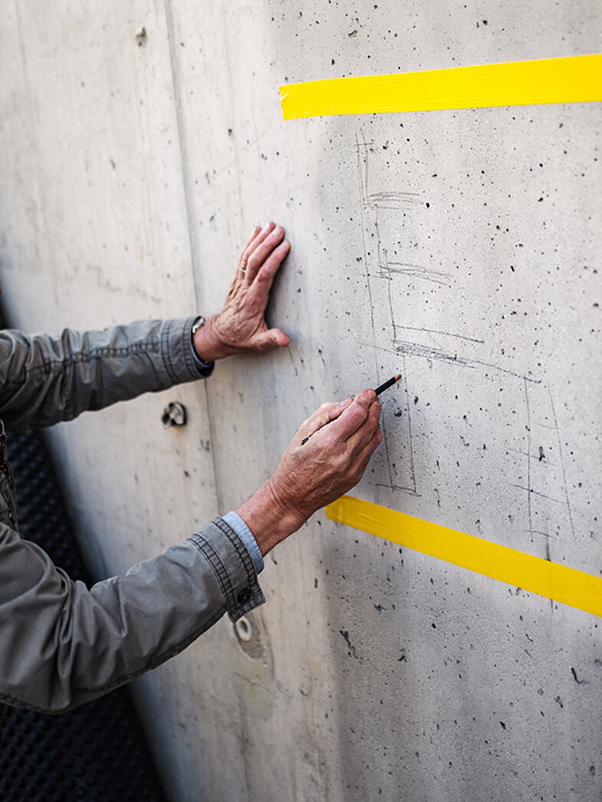 Gion A. Caminada draws a pencil diagram sketch on congrete walls bounded by two yellow lines | Alpine Architecture in Switzerland