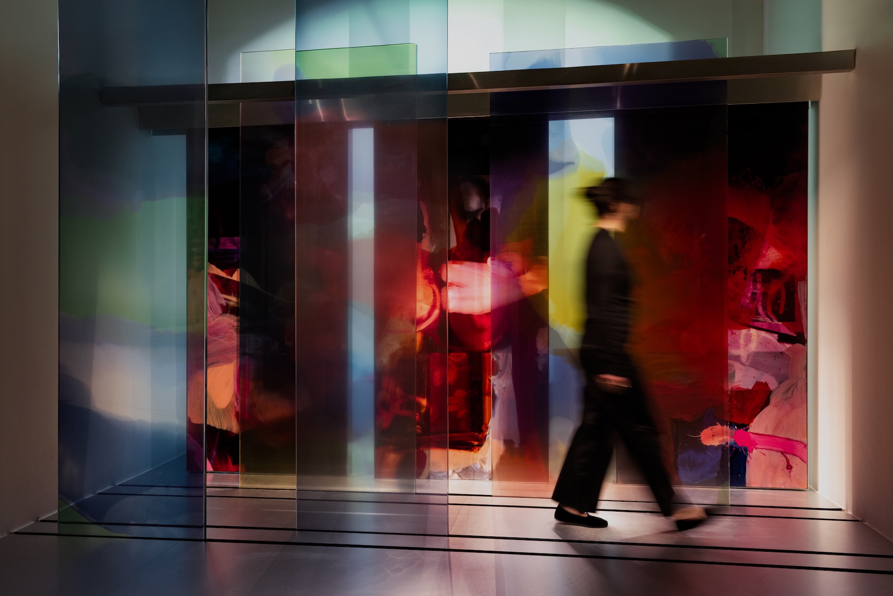  A visitor walks past layered transparent coloured panels set before a large abstract painting in red, pink and yellow by Draga & Aurel | The Aficionados