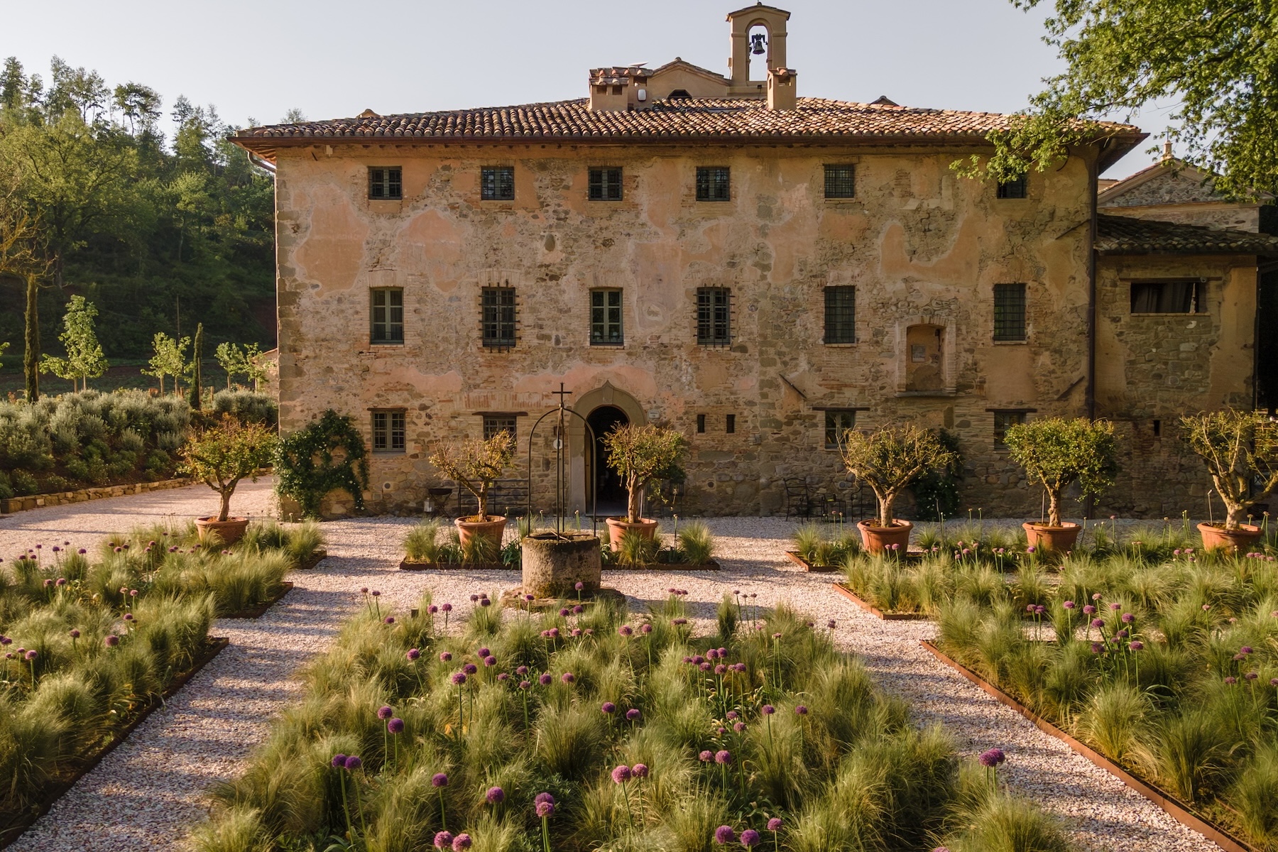 The honeyed-stone façade and bell-cote of Vocabolo Moscatelli, a former Umbrian monastery, above an allium garden and central stone well.