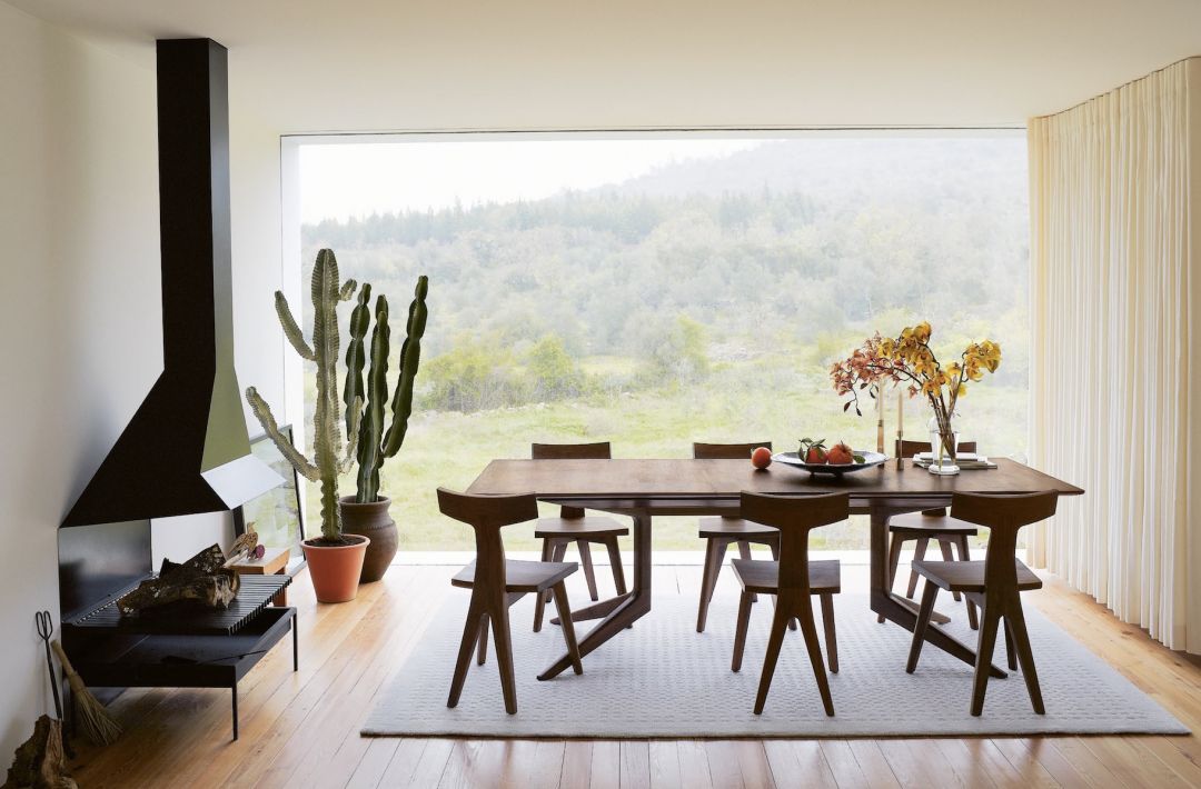 Solid walnut dining table and chairs by De La Espada in a hillside house with a sculptural black fireplace | The Aficionados