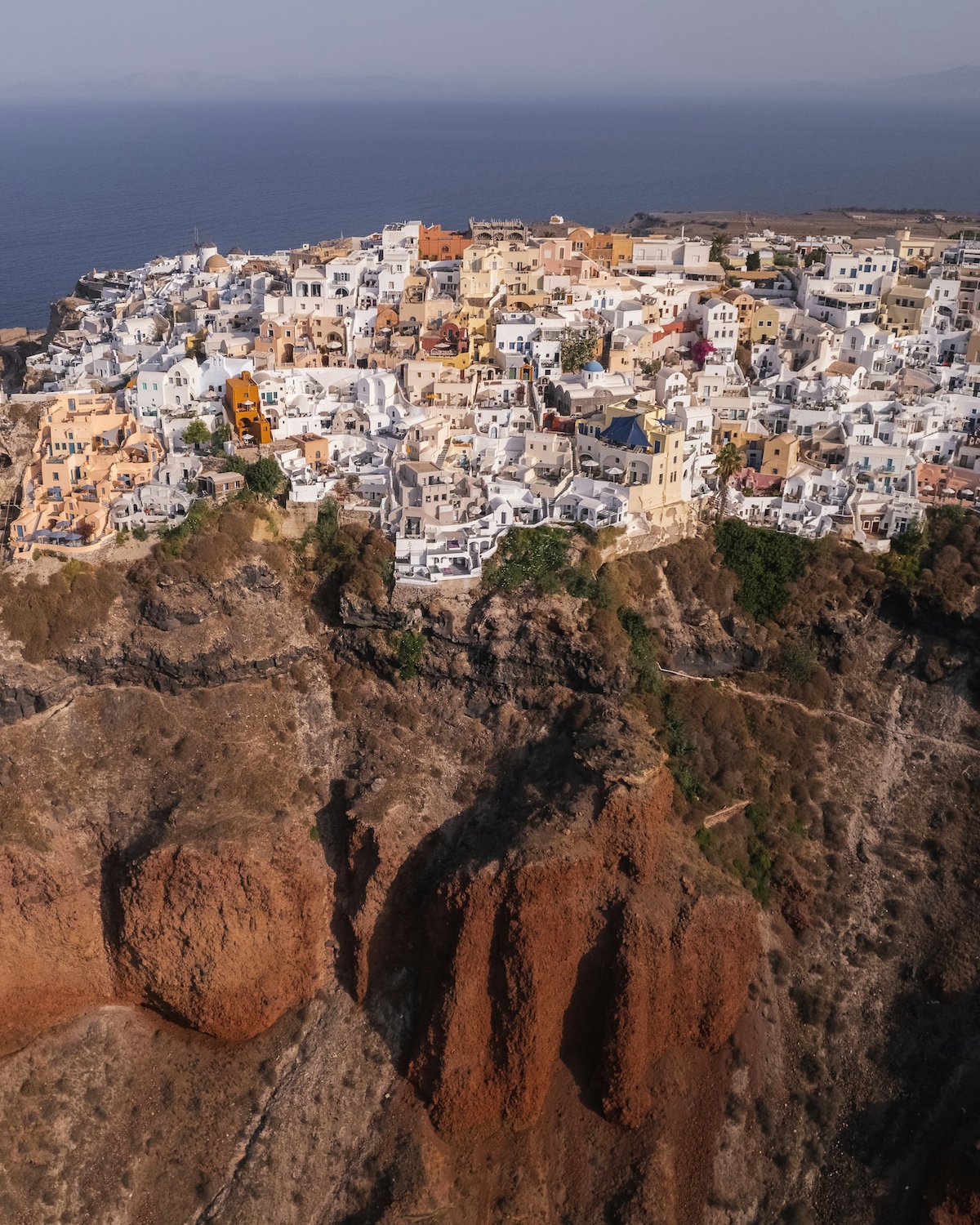 The clifftop village of Oia> white buildings hugging the edge of a cliffside overlooking the Caldera. |Santorini Noir: Volcanic Beauty, Architecture and Cycladic Soul| The Cyclades Island of Greece | The Aficionados 