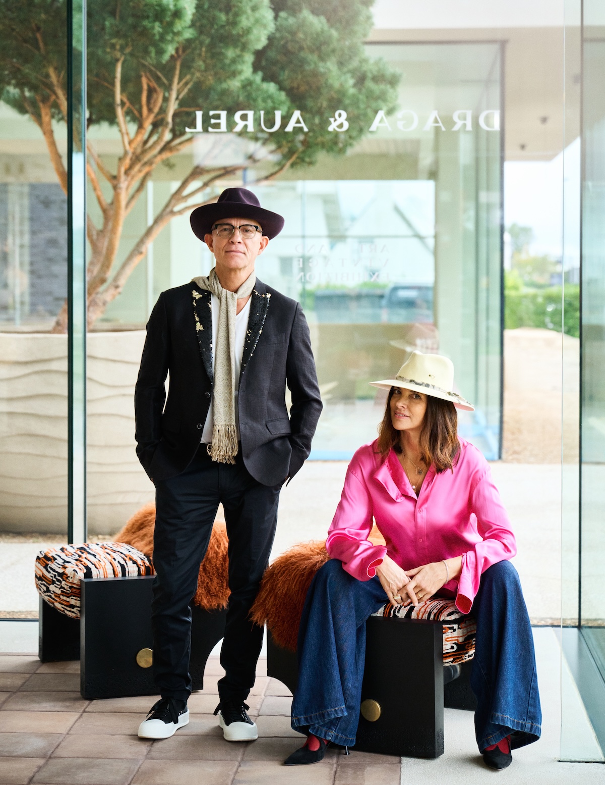 Aurel K. Basedow and Draga Obradovic in hats beside a glass window etched with the Draga & Aurel name | The Aficionados