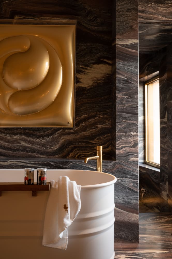 VENICE VENICE HOTEL. - White Stand alone bathtub against a marble wall with scultpured gold artwork - new luxury Bathroom desgin |Agape: Sculptural Bathroom Design Across Iconic Hotels | The Aficionados 