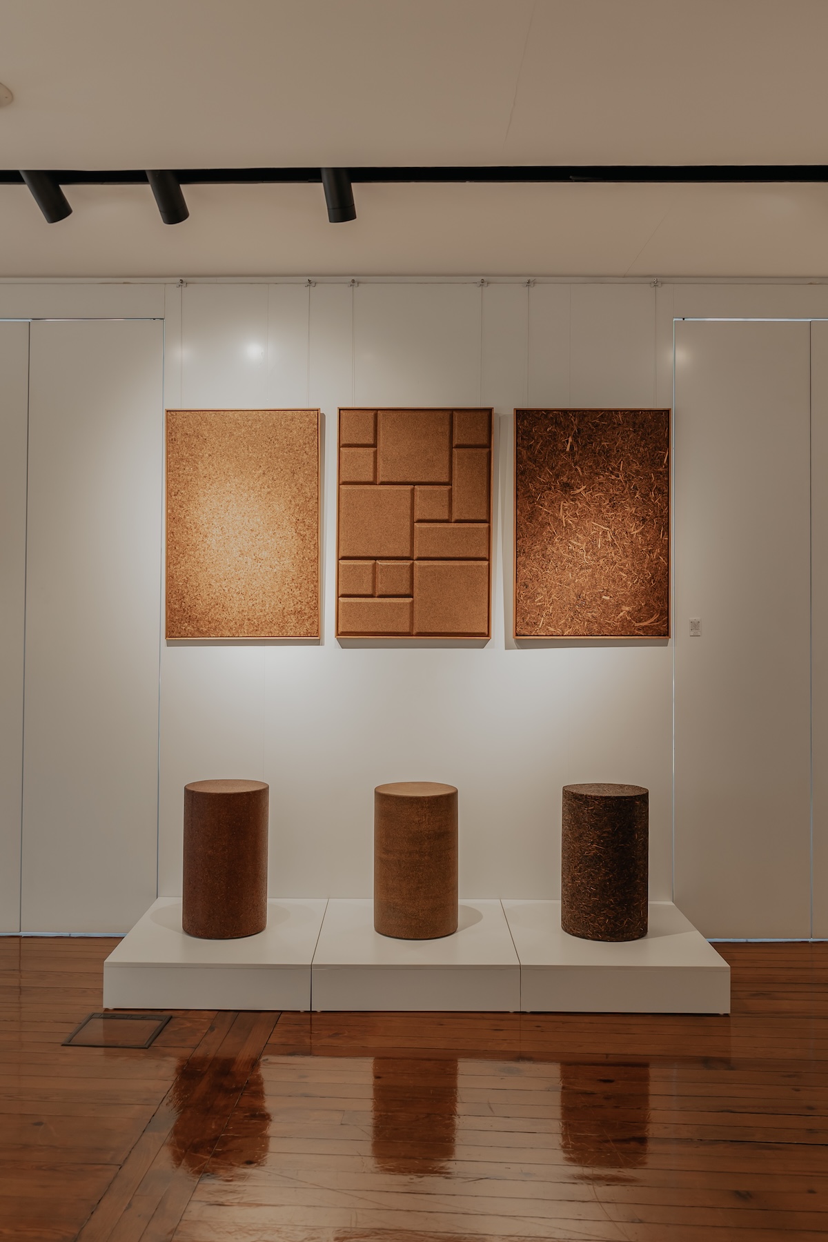 Three cork panel artworks and cork cylinder stools displayed in a gallery at Lisbon Design Week 2026