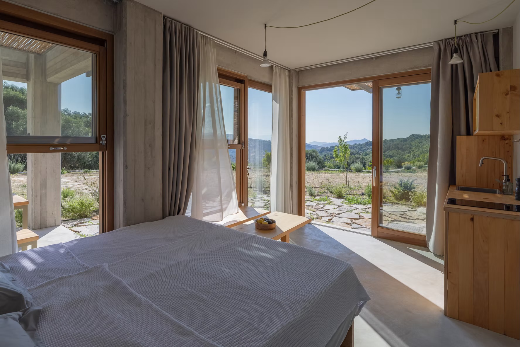 Self-catering apartment interior at Meraki Studios with a platform bed, kitchenette and full-height glazing onto the Cretan hills | The Aficionados