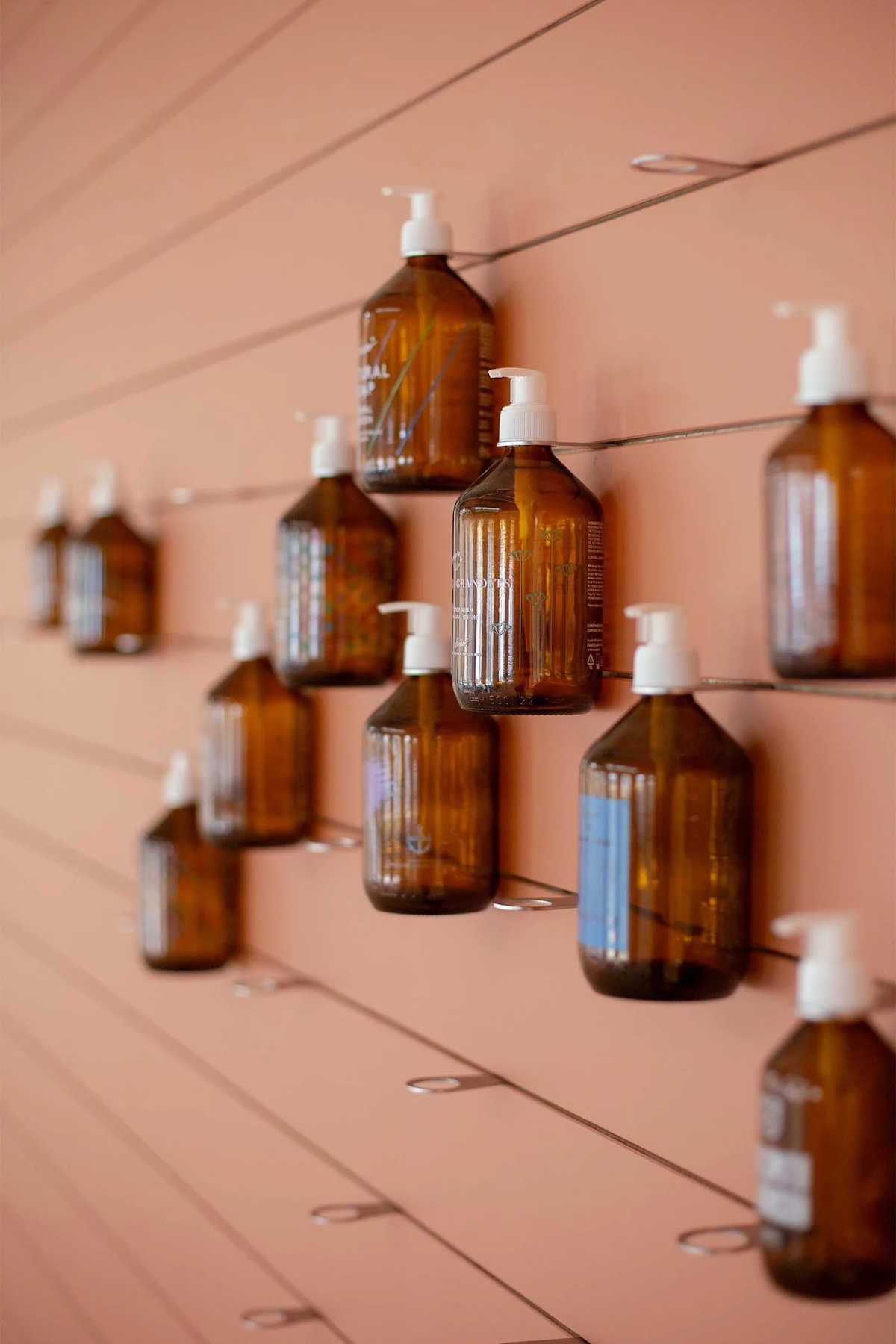 Soeder amber glass pump bottles mounted on a wire display against a blush-pink wall, refillable 100 per cent natural soap and body care, Zurich Switzerland | The Aficionados