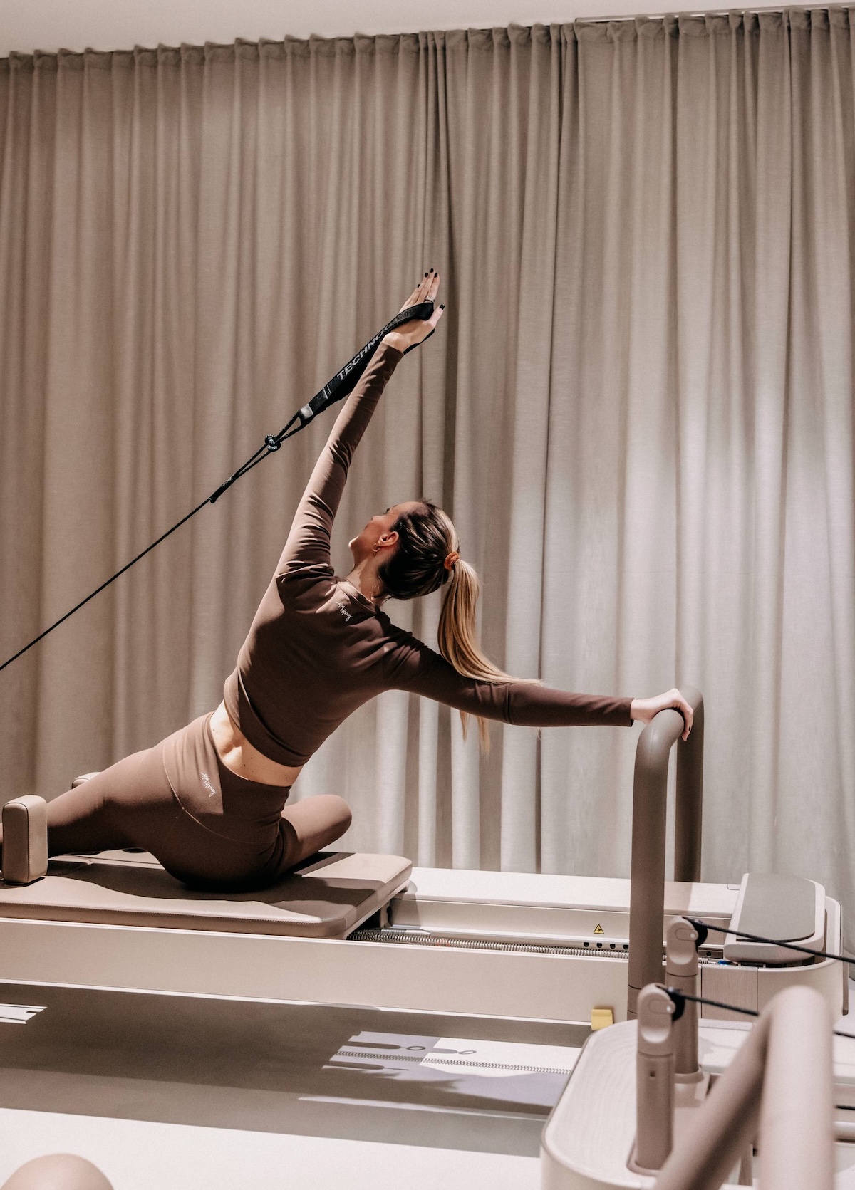 Guest in a kneeling side stretch on the reformer straps during a Reformer Pilates session at waldSPA Fitness, Naturhotel Forsthofgut, Leogang, Salzburger Land, Austria | The Aficionados.