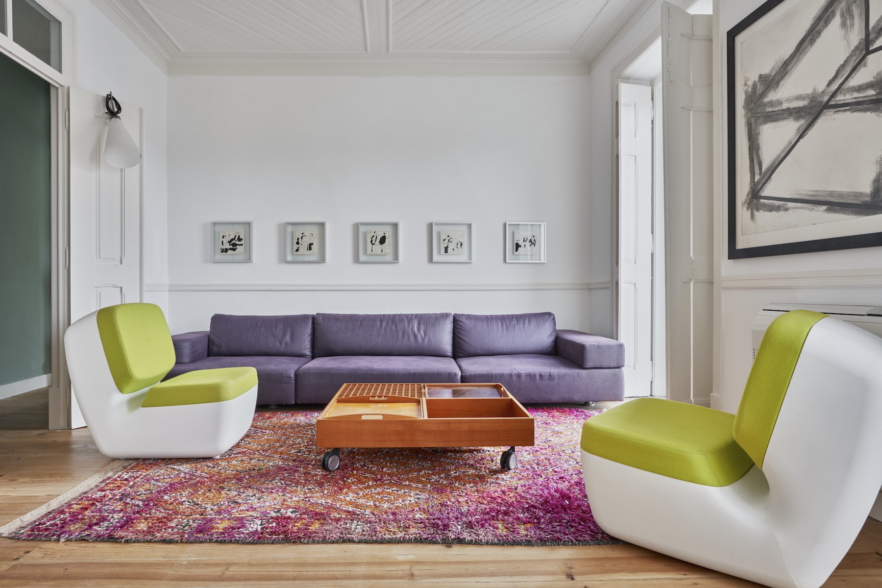 A colour-led sitting room at Casa Fortunato, Alentejo, with a lilac sofa, lime-green chairs and a row of framed drawings above a magenta rug.