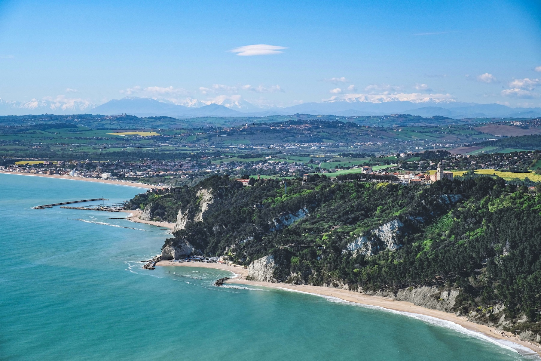 Aerial view of the Le Marche coastline with cliffs, sandy beaches and snow-capped Apennines behind