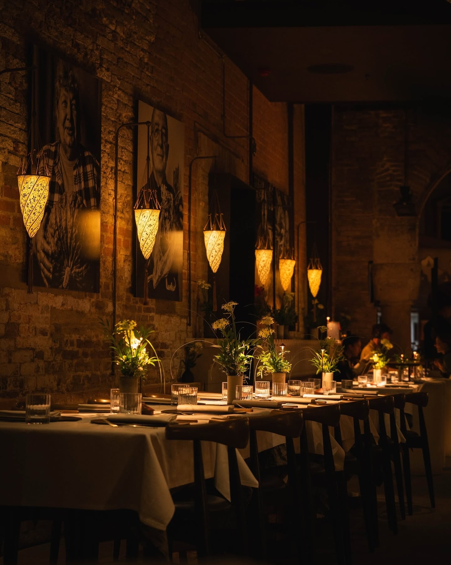 Long communal table at Francy's beneath Fortuny lanterns, exposed brick and black-and-white portraits.