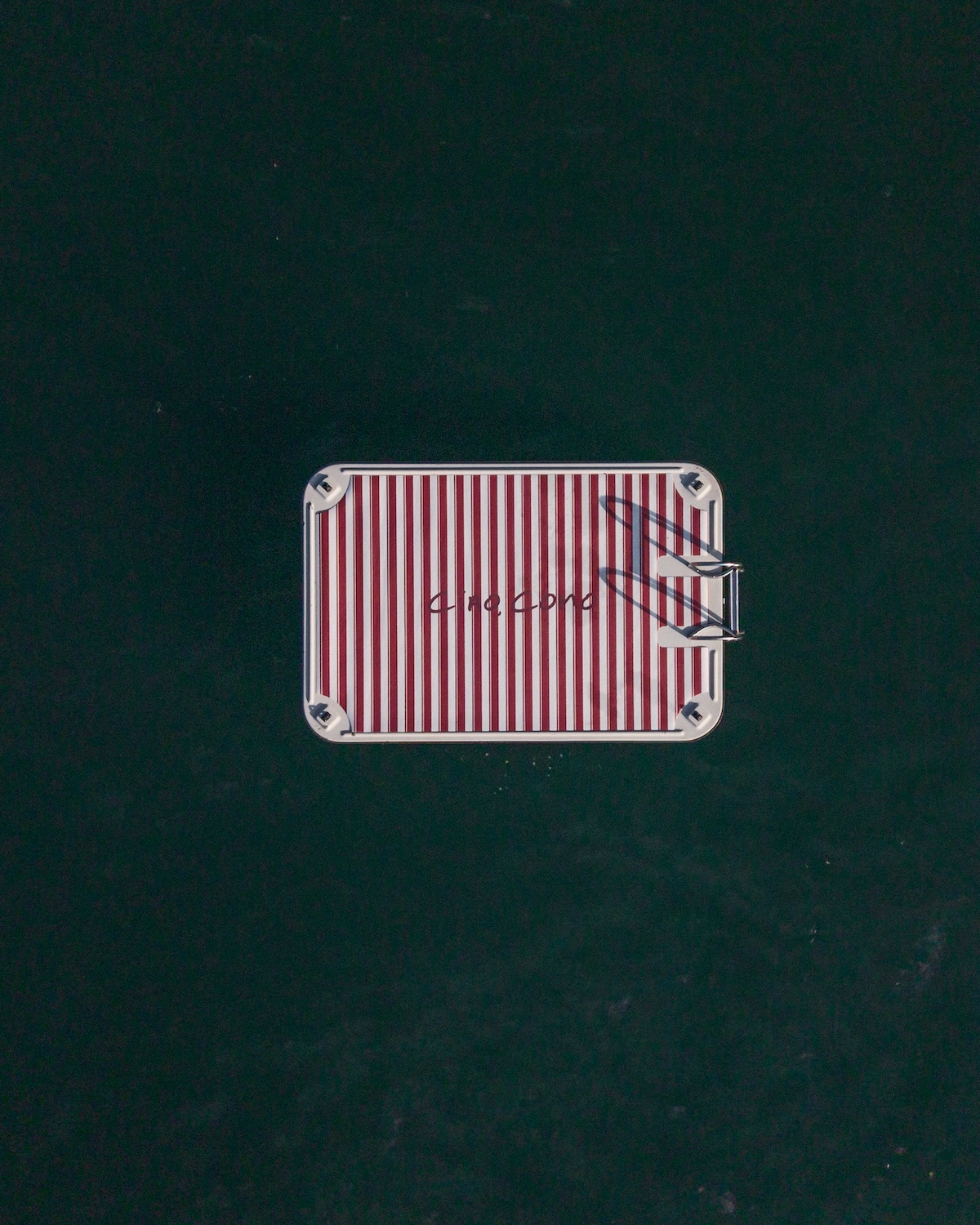 Aerial view of red-and-cream striped floating platform with Ciao Como script on dark Lake Como water, Filario lido, GUESS collaboration | TheAficionados.com