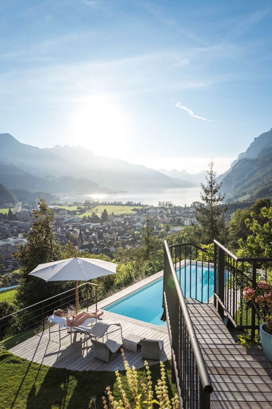 Guest relaxing by the outdoor pool at Hasenberg Lodge, wooden deck overlooking the valley and Lake Walen below.