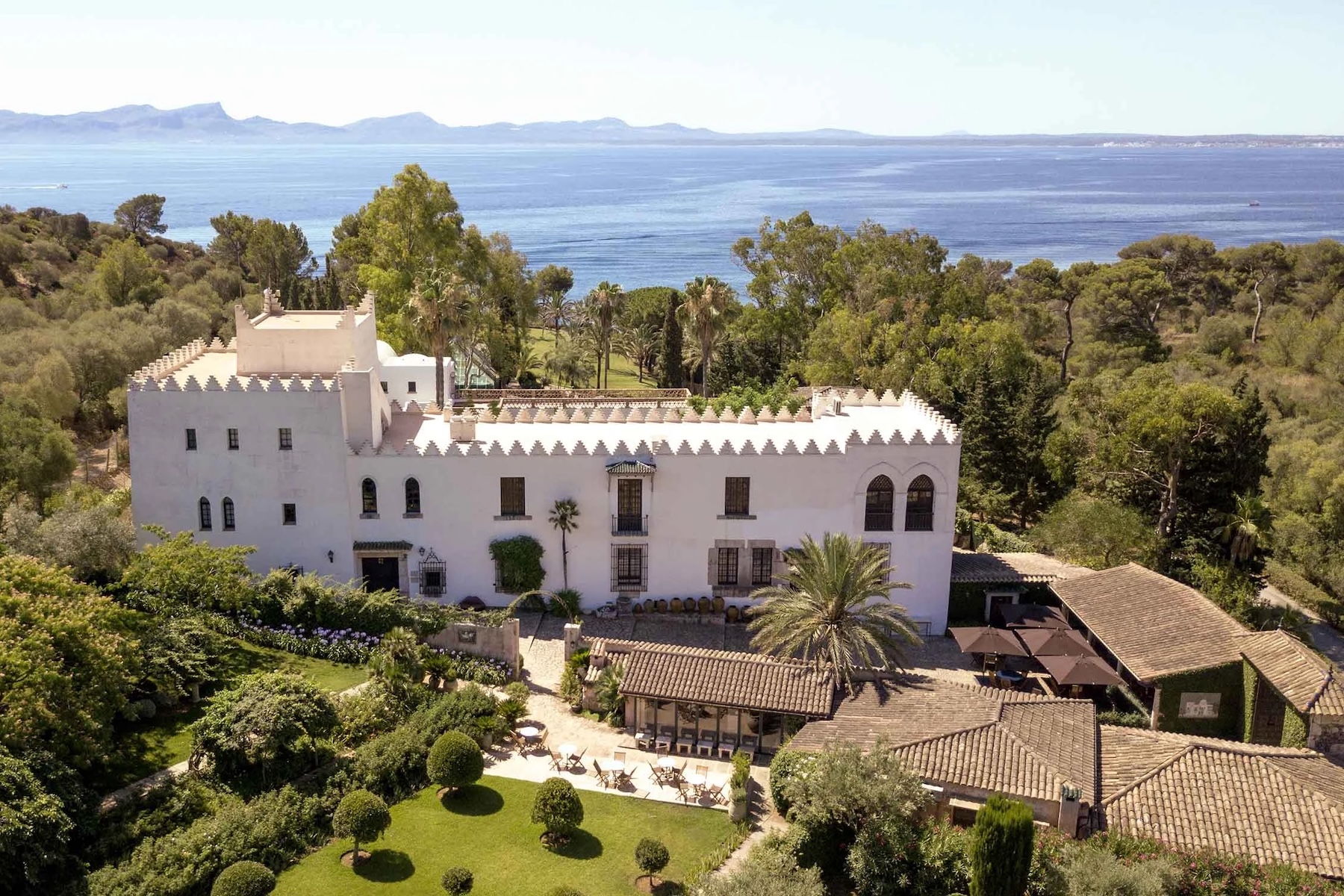 Aerial view of Sa Bassa Blanca above Alcúdia, a white crenellated Hispano-Moorish house in woodland above the bay | The Aficionados