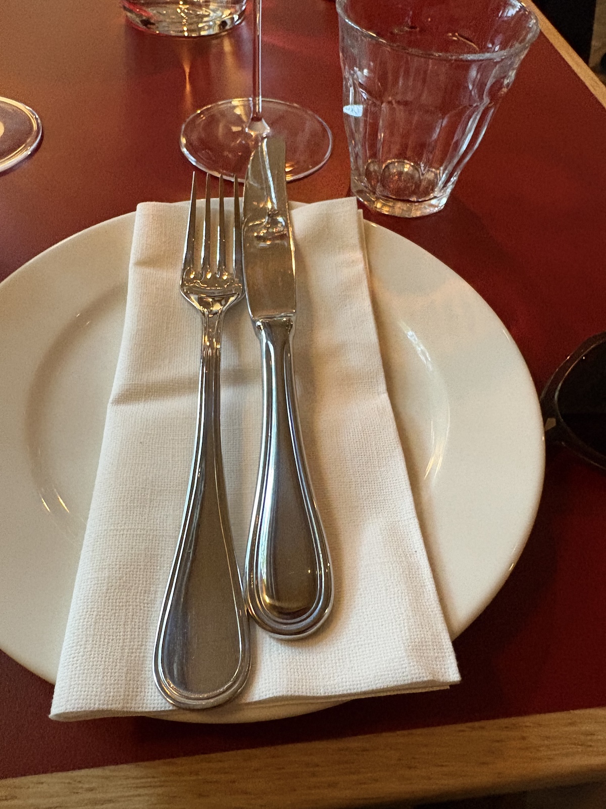 Linen napkin and silver cutlery on a white plate at Donauhof, set against an oxblood tabletop