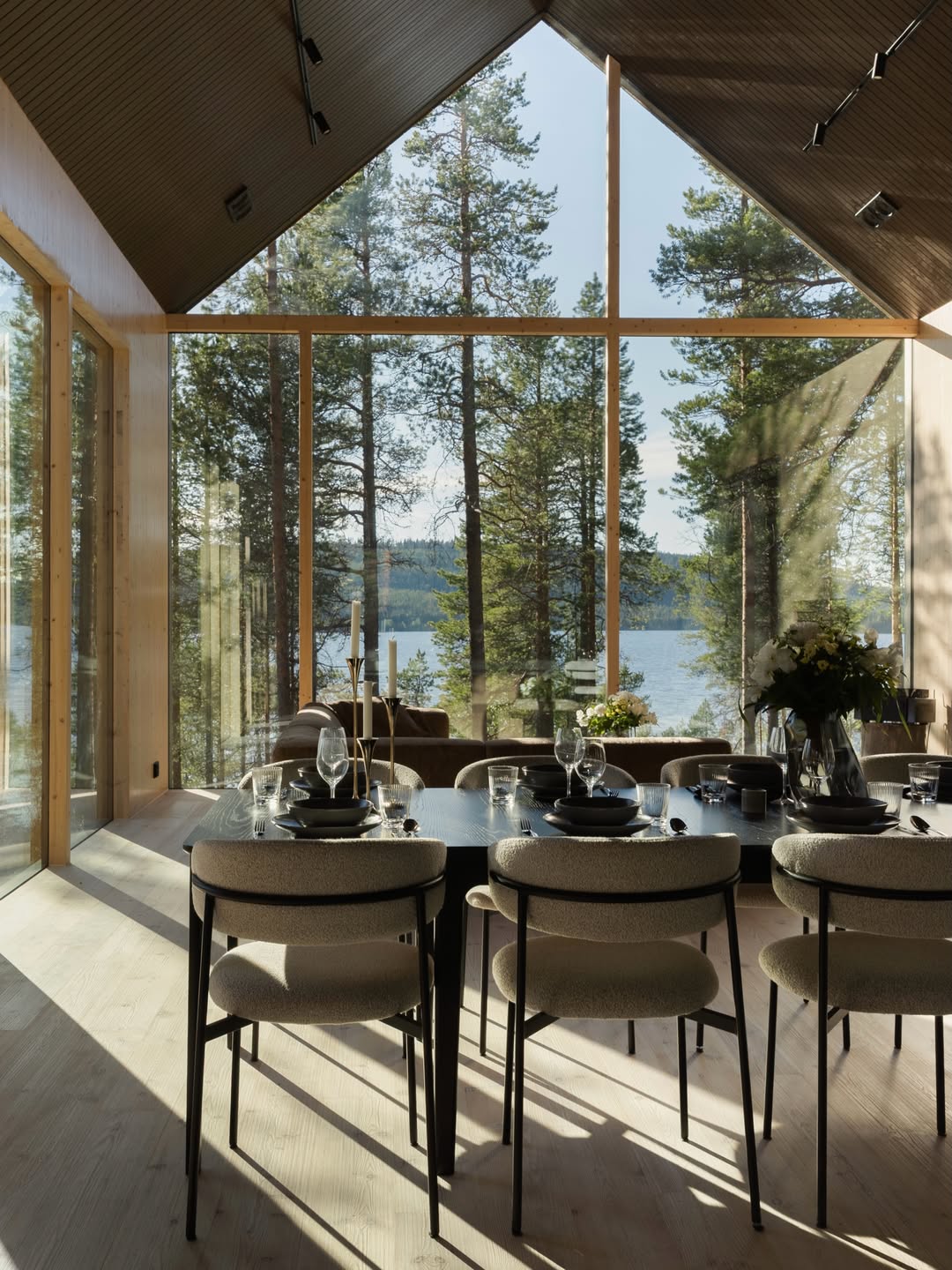 Dining table beneath a pitched timber ceiling with gable glazing onto the lake and pines | Inai Haven, Lake Inari, Lapland, Finland | The Aficionados