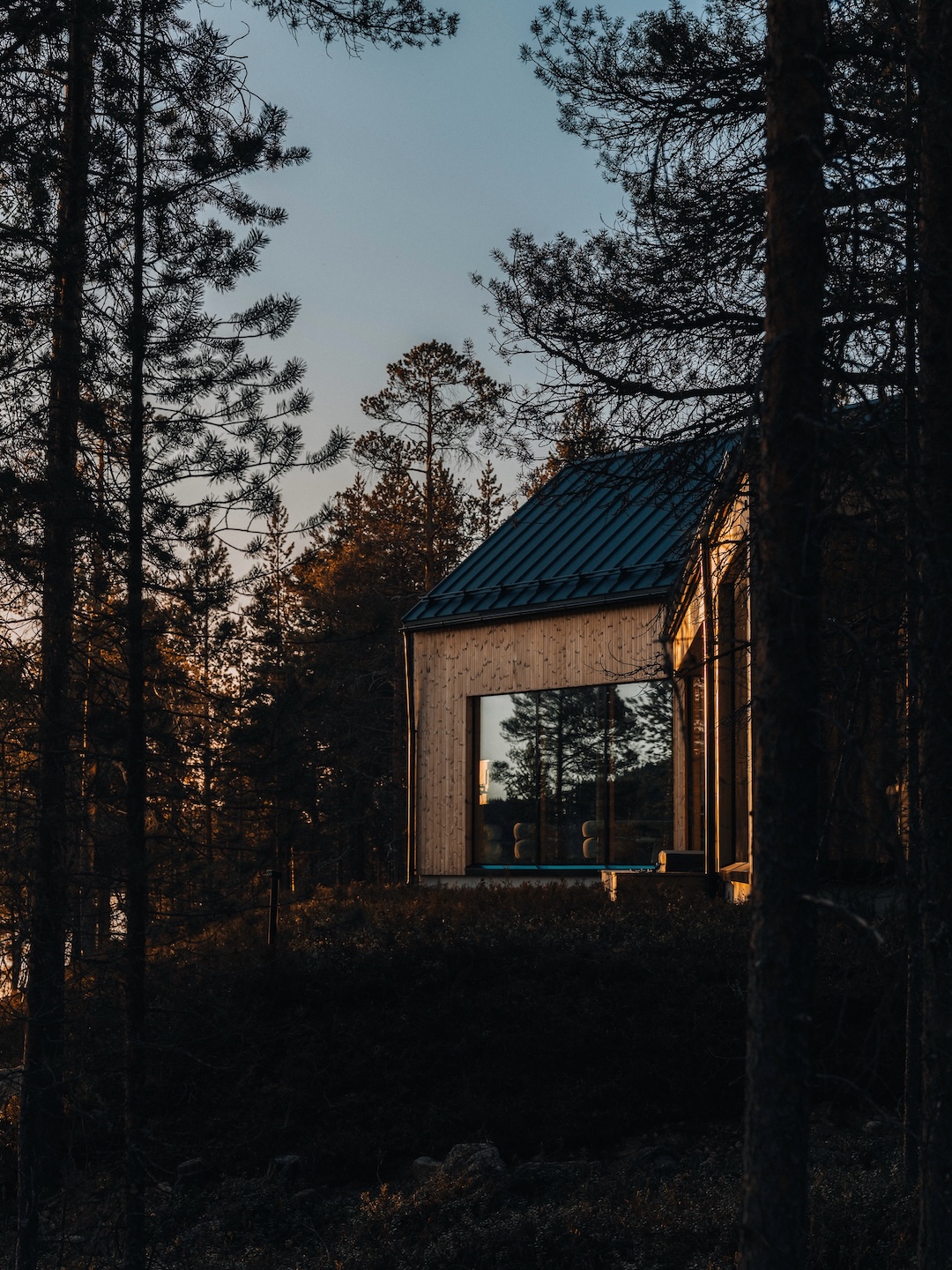 Timber villa glowing through the pine forest at dusk, by Kati Anglé and Tapani Takkunen | Inai Haven, Lake Inari, Lapland, Finland | The Aficionados