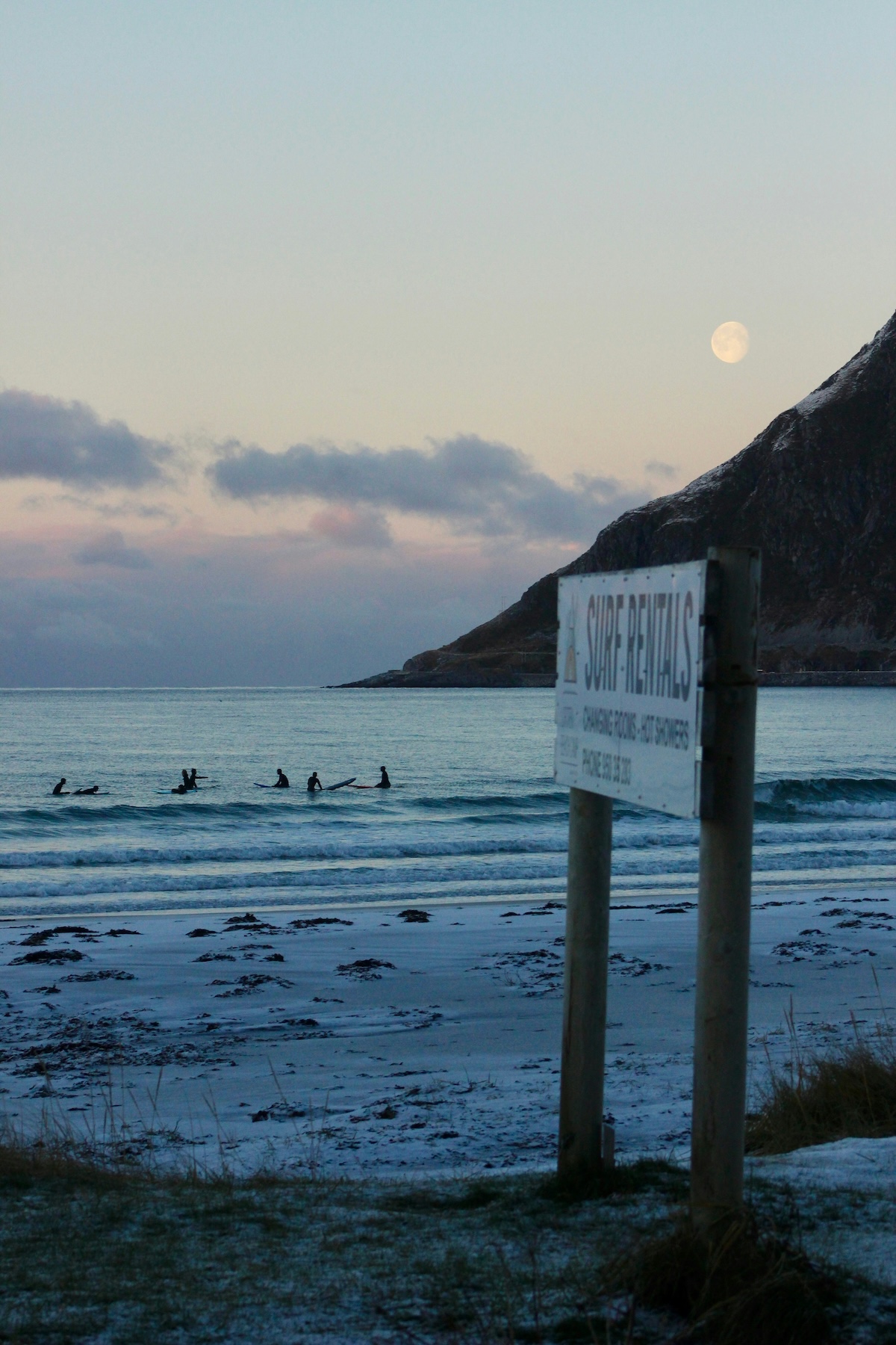 Lofoten Beach: Arctic Surf of Flakstad, White Sand and Midnight Sun | Surfers in the sea, blue waters, moddy skies | The Aficionados 