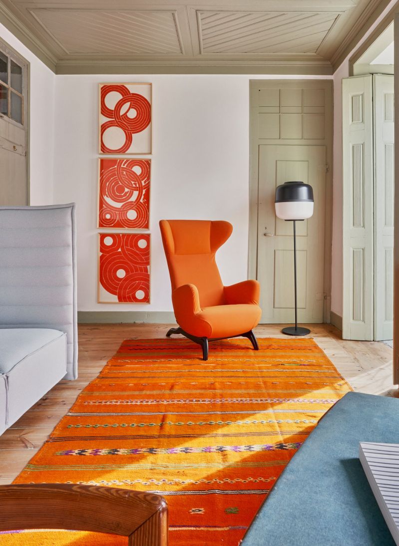 Mid Century Chair in orange against an organe rug and abstract artwork and a Vitra Sofa | Design Hotel Alentejo Casa Fortunato |Poetic Design Hotels & Creative Hideaways Across Europe – The Aficionados