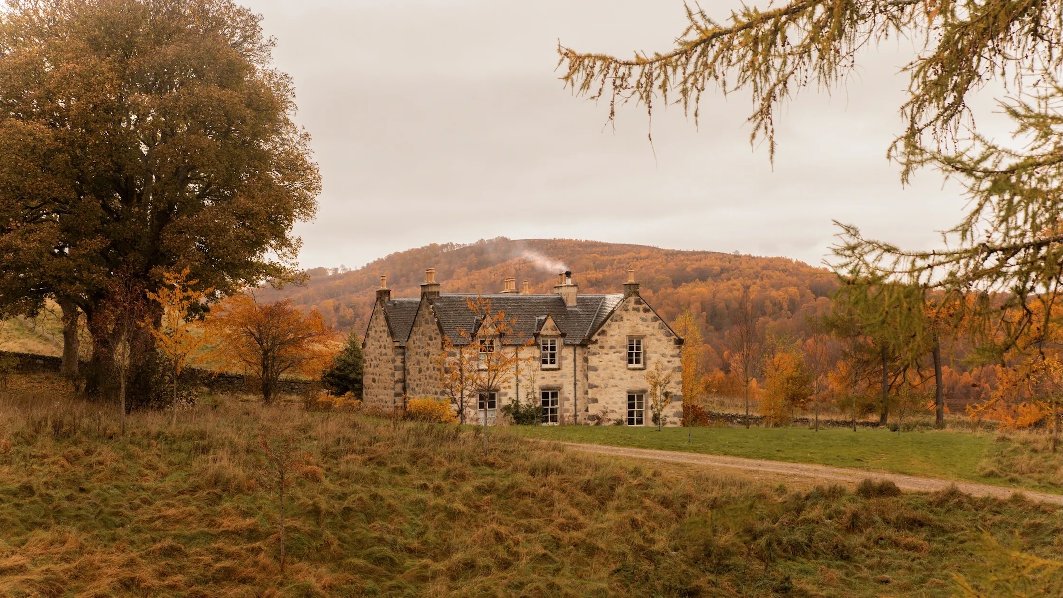 Killiehuntly Farmhouse near Kingussie, a whitewashed stone Highland farmhouse with a smoking chimney, set in autumn woodland and moor in the Cairngorms.
