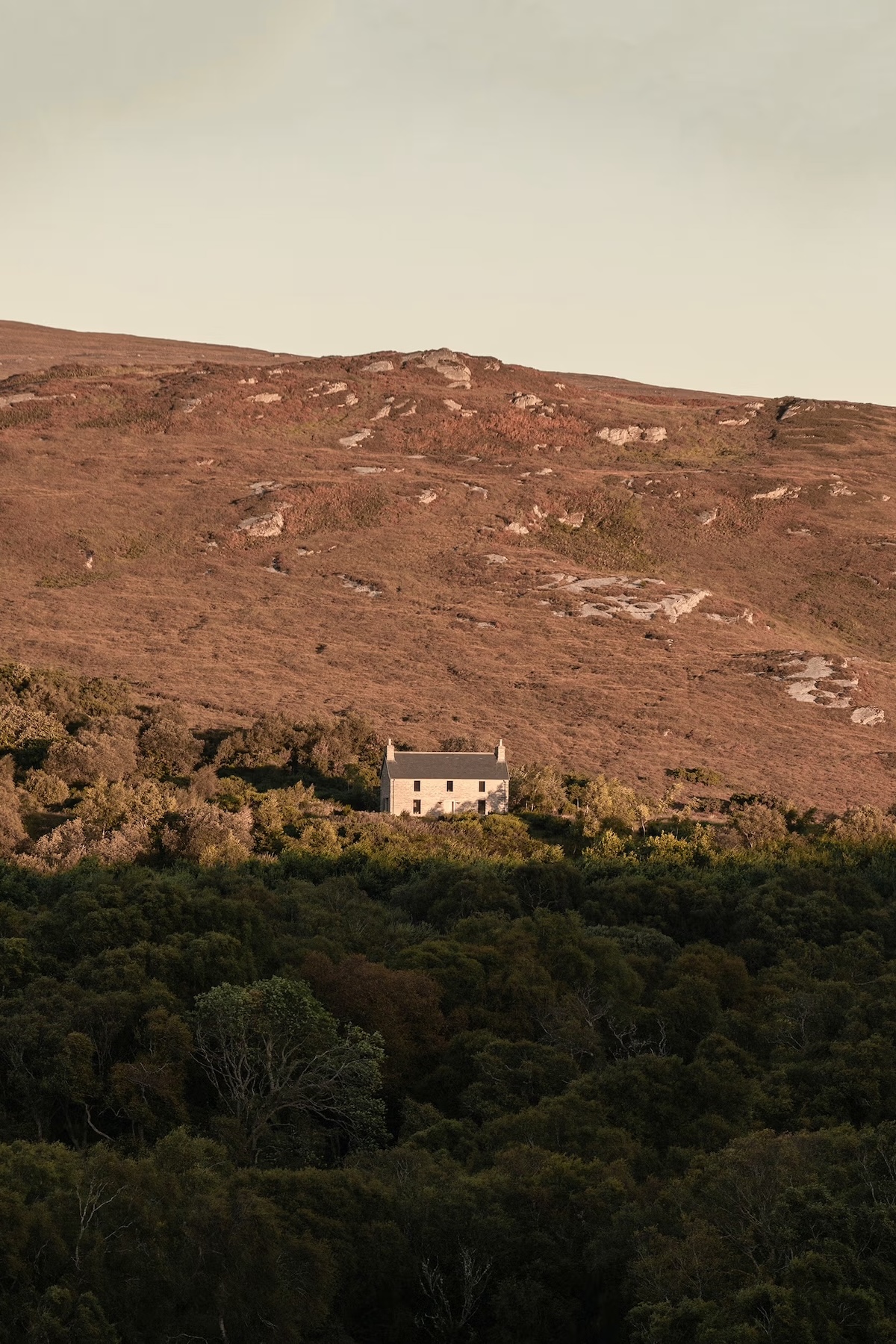 Kyle House Sctoland A lone stone Highland house among woodland below open moorland in golden evening light, Sutherland, Scotland.