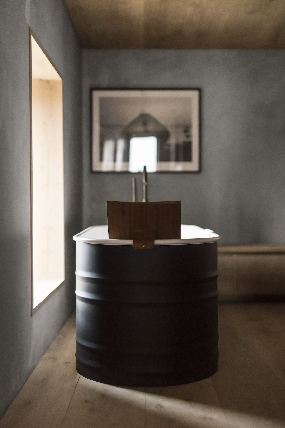 AGAPE statmeent bathtub in bakc metal cathing sunlight at the Scottish Kyle House with concrete walls and wooden flooring: Bathroom desgin | Agape: Sculptural Bathroom Design Across Iconic Hotels | The Aficionados 
