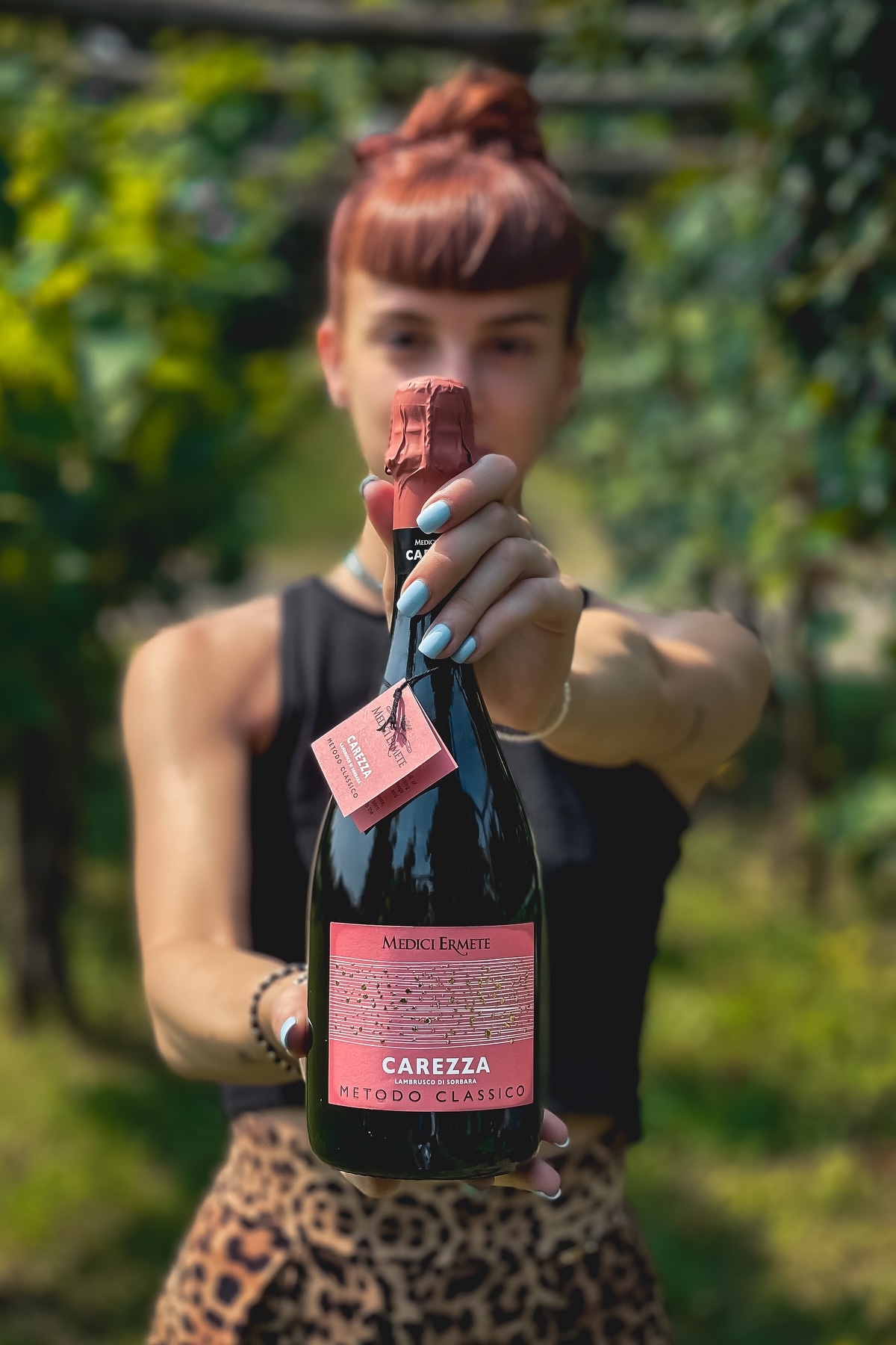 A bottle of Medici Ermete Carezza Lambrusco Metodo Classico held out to camera in an Emilia-Romagna vineyard | The Aficionados