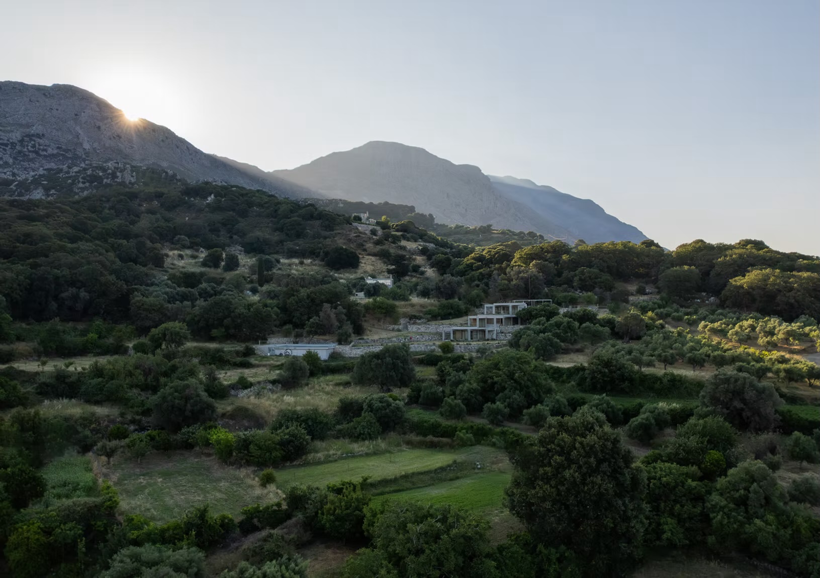Meraki Studios nestled in a hillside of olive groves near Kissos, Crete, a design retreat of concrete and local stone beneath the mountains at sunrise.