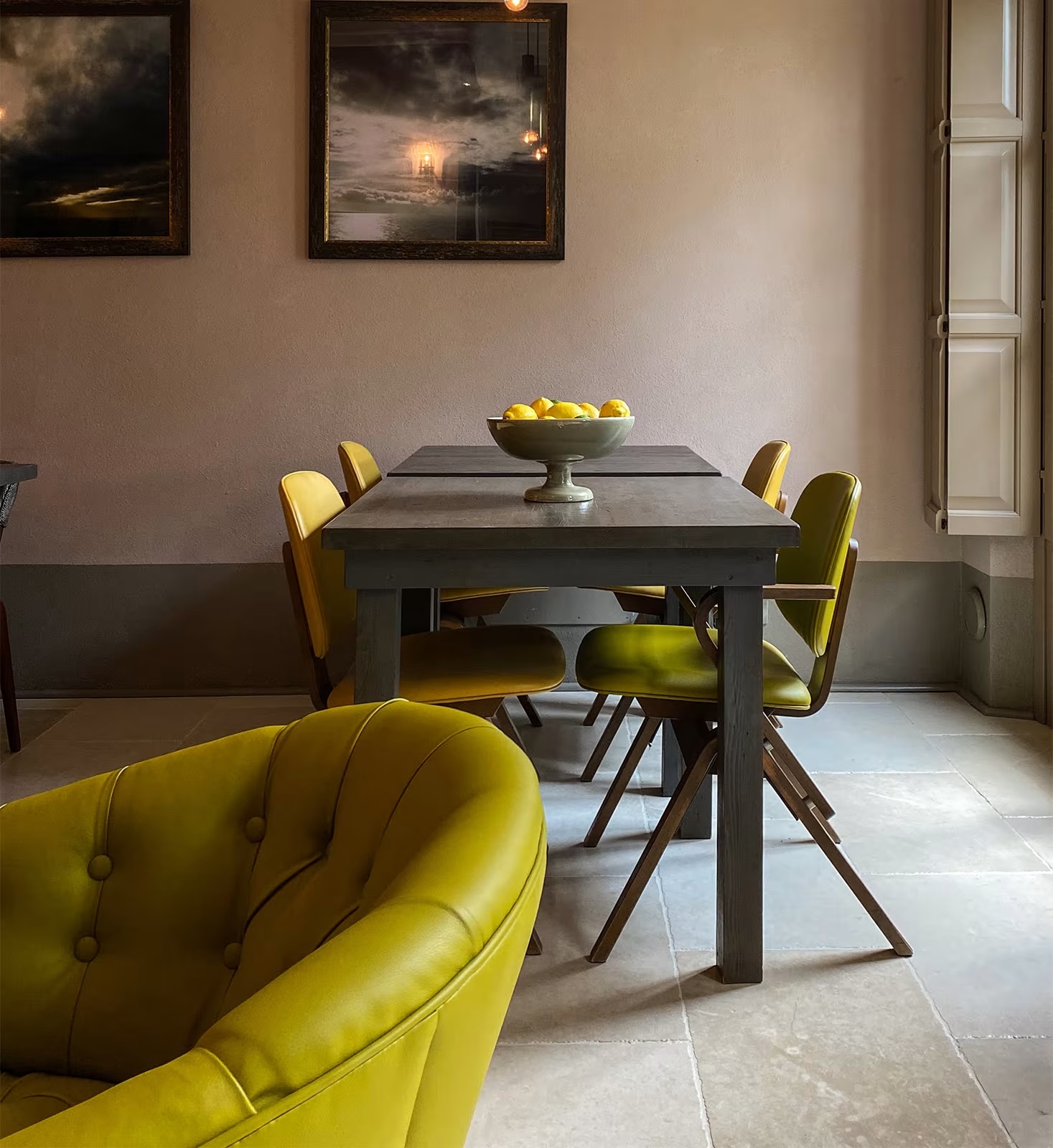Dining room at Locanda al Colle with chartreuse leather chairs, a grey table set with lemons and two dark seascapes above | The Aficionados