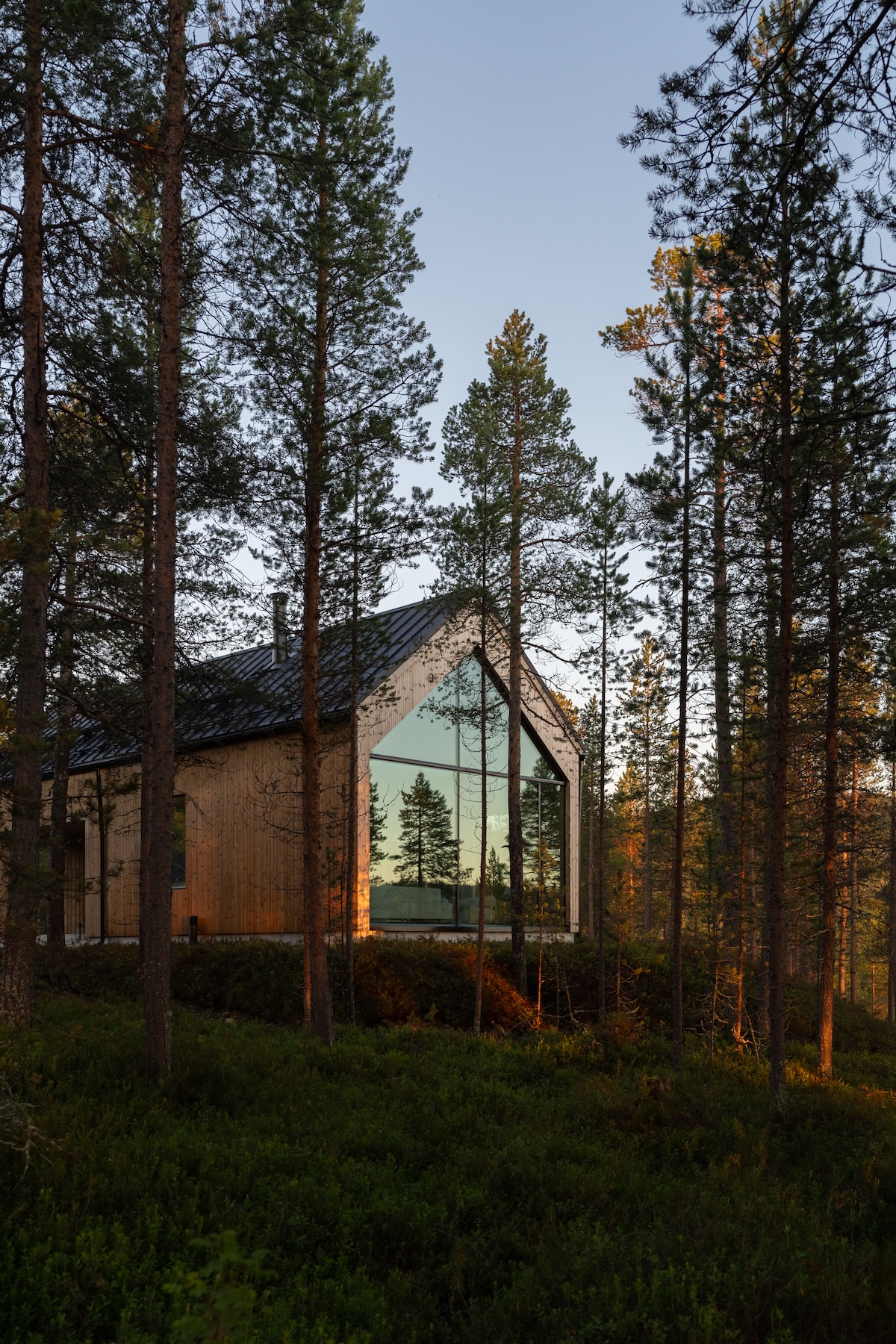Timber villa glowing through the pine forest at dusk, by Kati Anglé and Tapani Takkunen | Inai Haven, Lake Inari, Lapland, Finland | The Aficionados