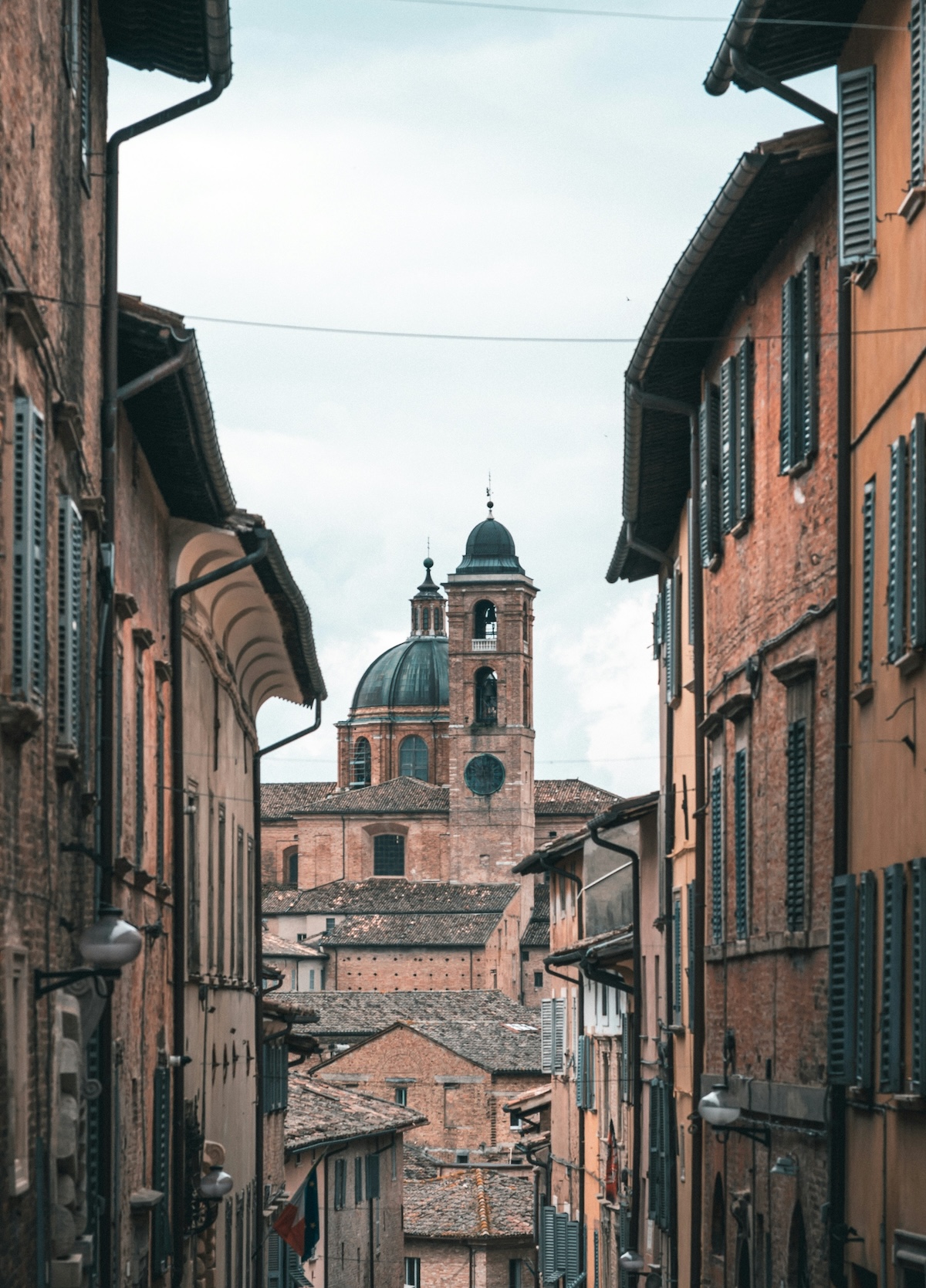 Cathedral dome and bell tower framed by a narrow terracotta street in Urbino, Le Marche Italy