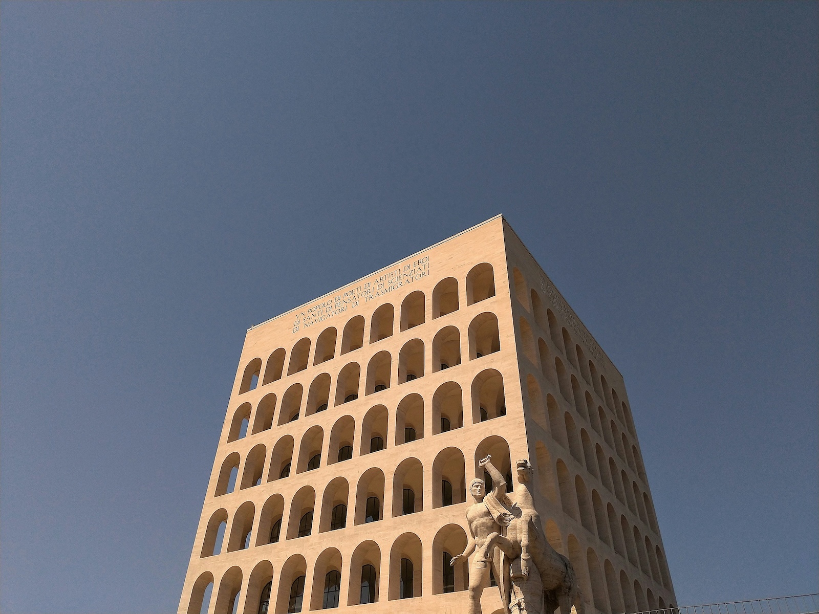 Looking up at the travertine arches of Rome's rationalist Palazzo della Civiltà Italiana against a deep blue sky
