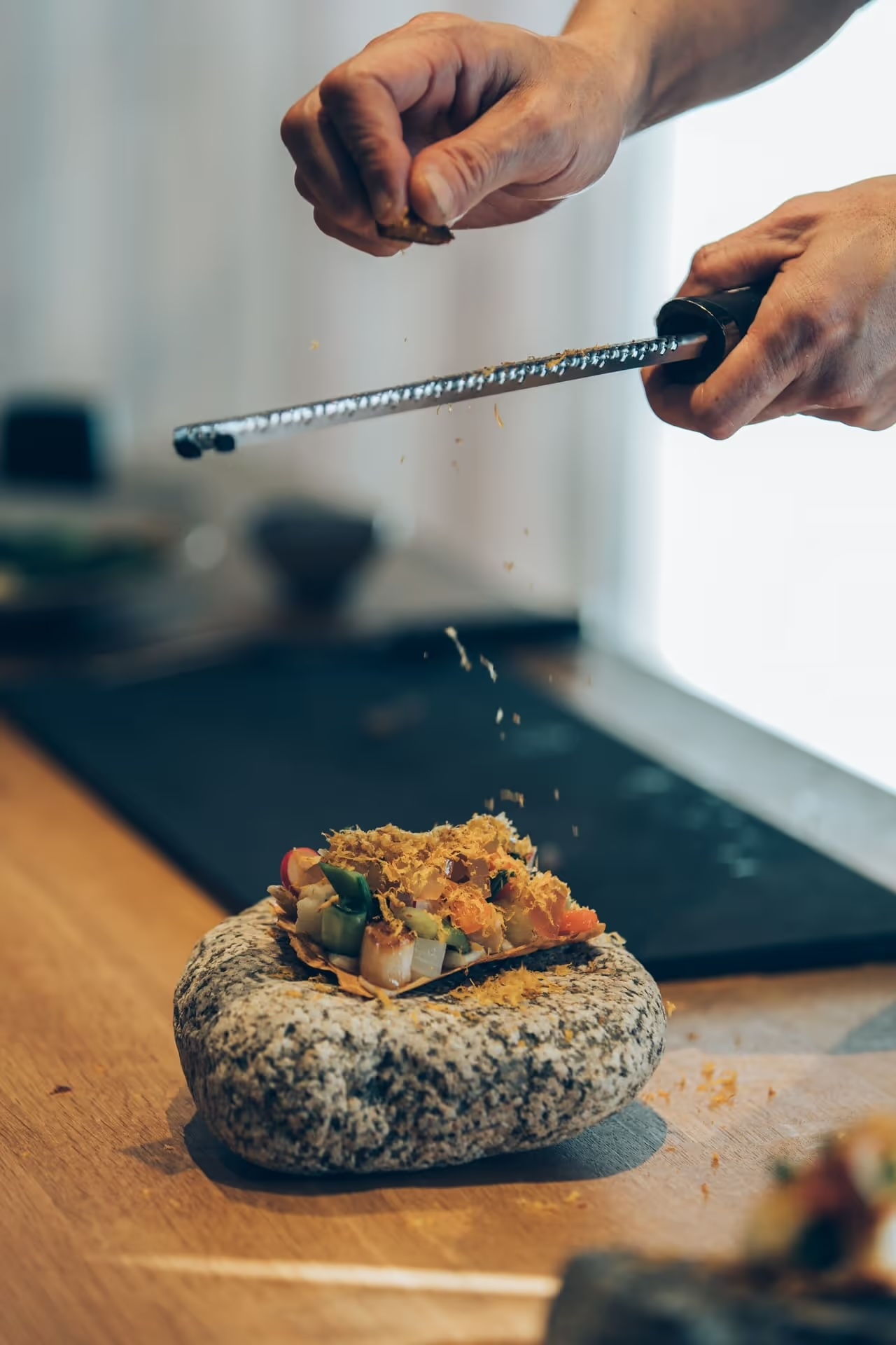 Makoto Fuse grating a golden topping over vegetables served on a granite stone at Auberge Né | The Aficionados