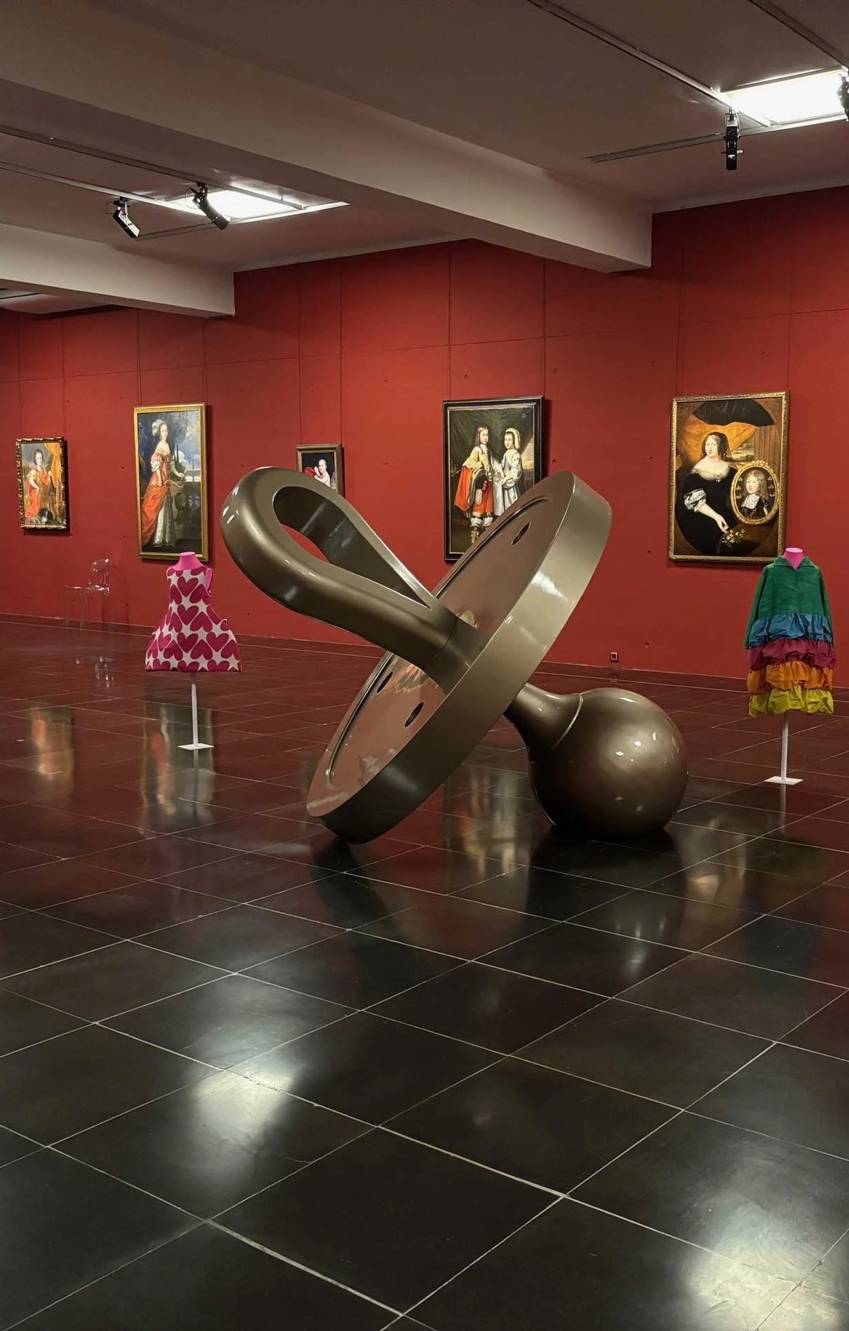 A red-walled gallery hung with historic portraits, a large bronze sculpture set on the dark stone floor | The Aficionados