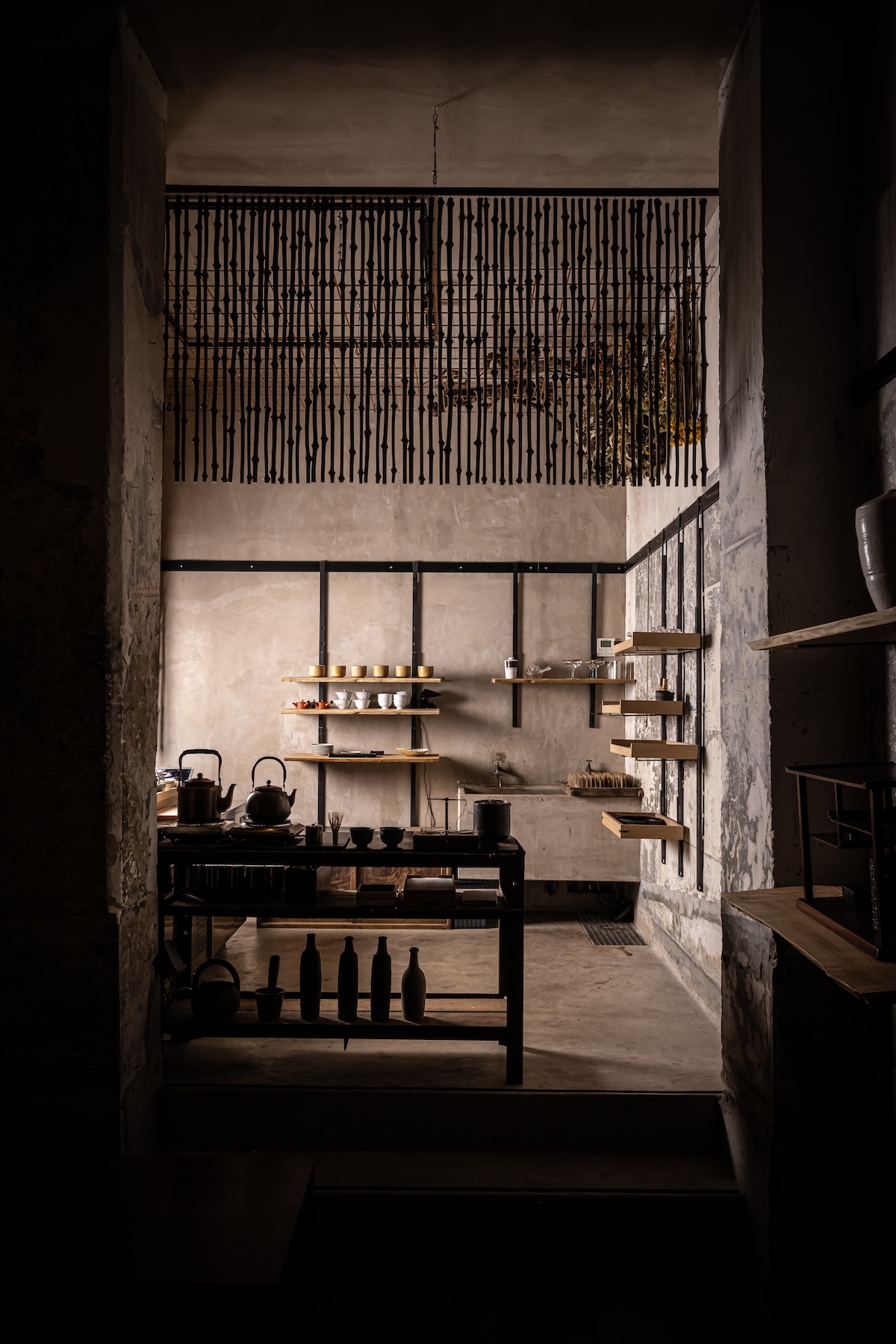 A doorway onto a tea preparation room with kettles, timber shelves and a ceiling hung with dark twigs | The Aficionados