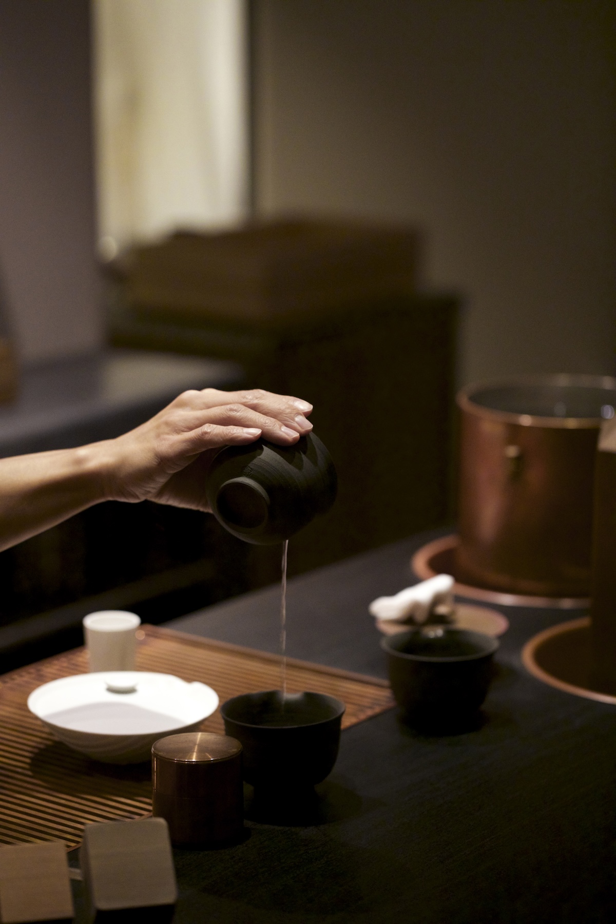 Tea poured from a dark pot into small cups beside copper vessels and a wooden caddy, a SIMPLICITY tea service | The Aficionados