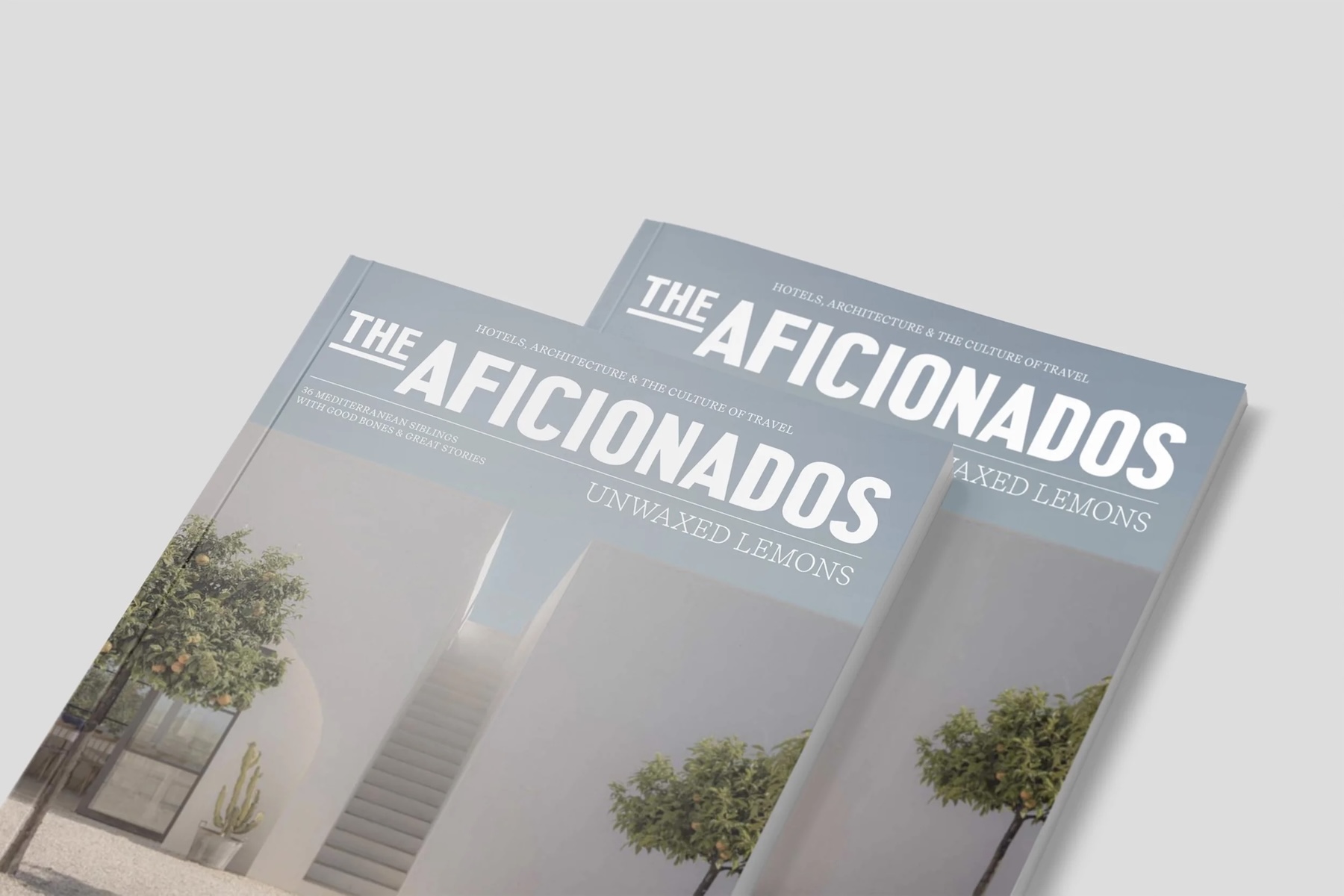 Two copies of Unwaxed Lemons, The Aficionados' print magazine of Mediterranean design hotels, on a pale grey surface | The Aficionados