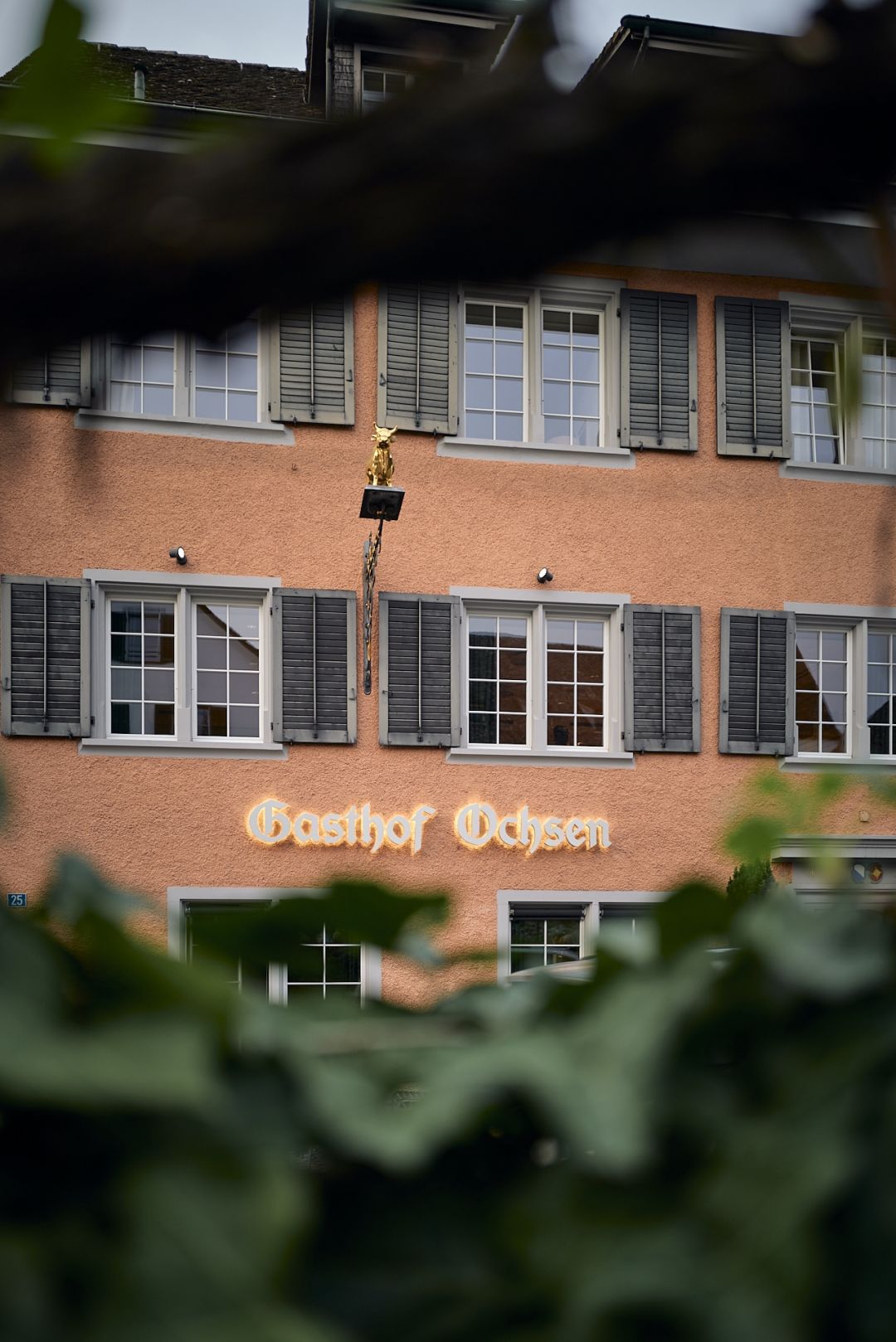 Facade of Gasthof Ochsen in Küsnacht with its gilded golden ox sign and grey shutters, on Zürich's Gold Coast.