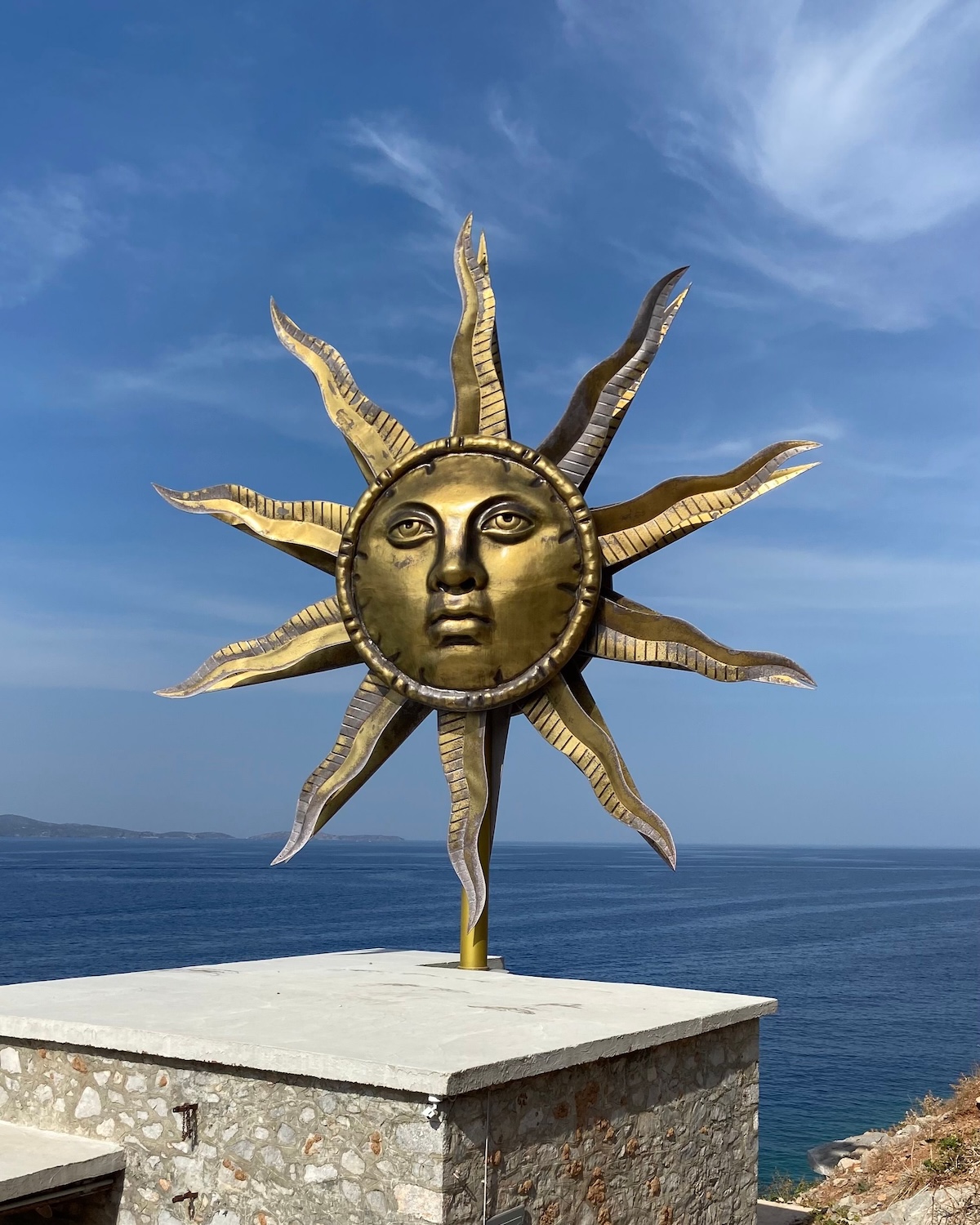 Gilded sun sculpture with a human face above the Aegean on Hydra | The Aficionados