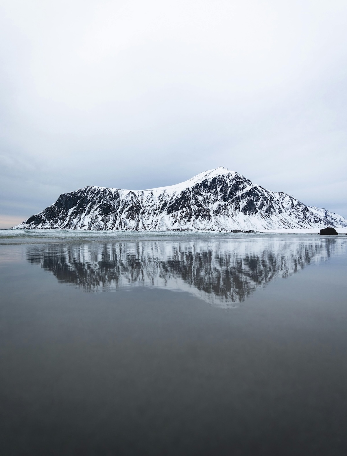 Lofoten Beach: Arctic Surf of Flakstad, White Sand and Midnight Sun | Surfers in the sea, blue waters, moddy skies | The Aficionados 