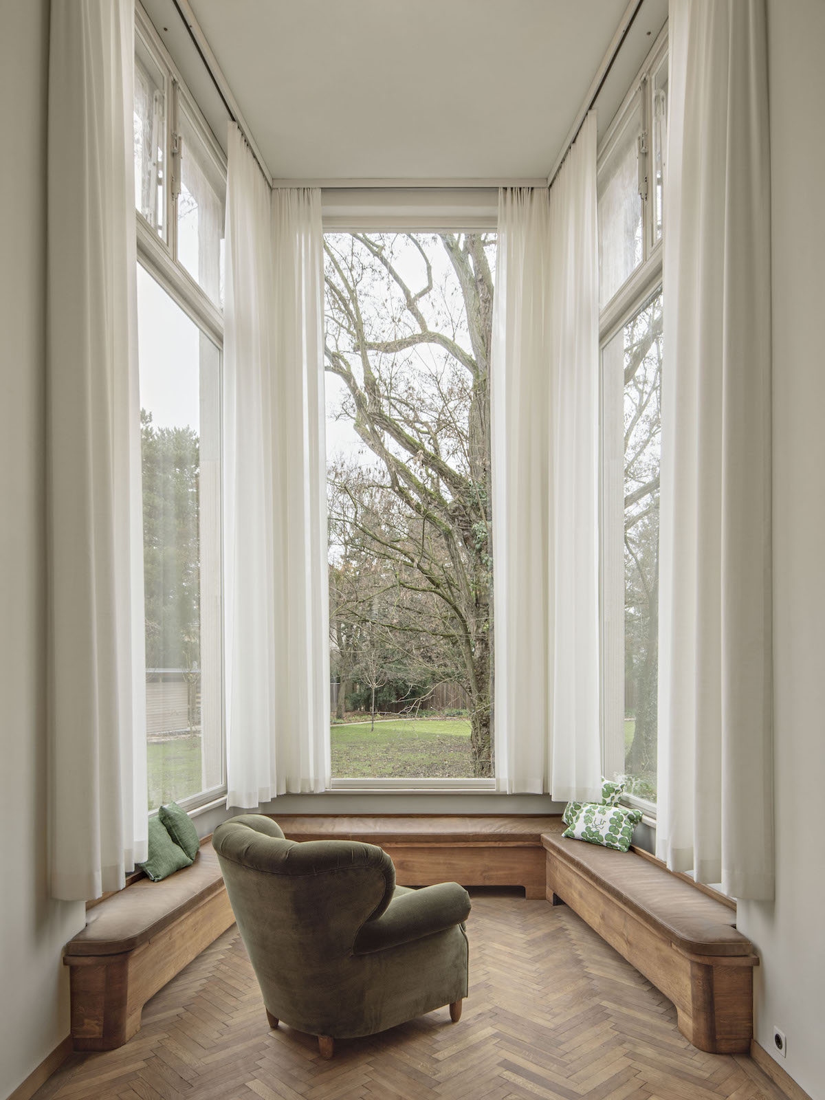 Villa Beer by Josef Frank | Sunlit bay window with a vintage armchair and tall white sash windows overlooking bare winter trees in a restored Viennese modernist interior