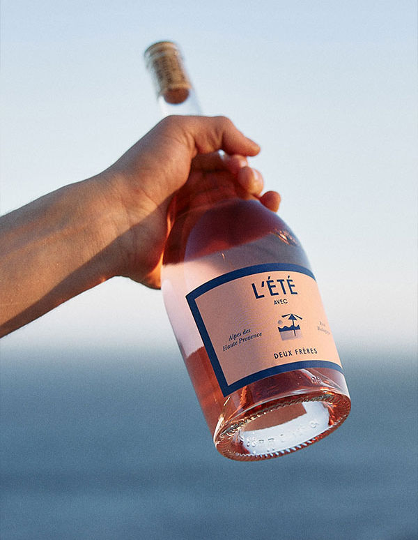Bottle of Rose held in a hand against the blue fo the sea and blue sky | Deux Frères Gin: Zurich’s Pink-Hued Rebels of Distilling