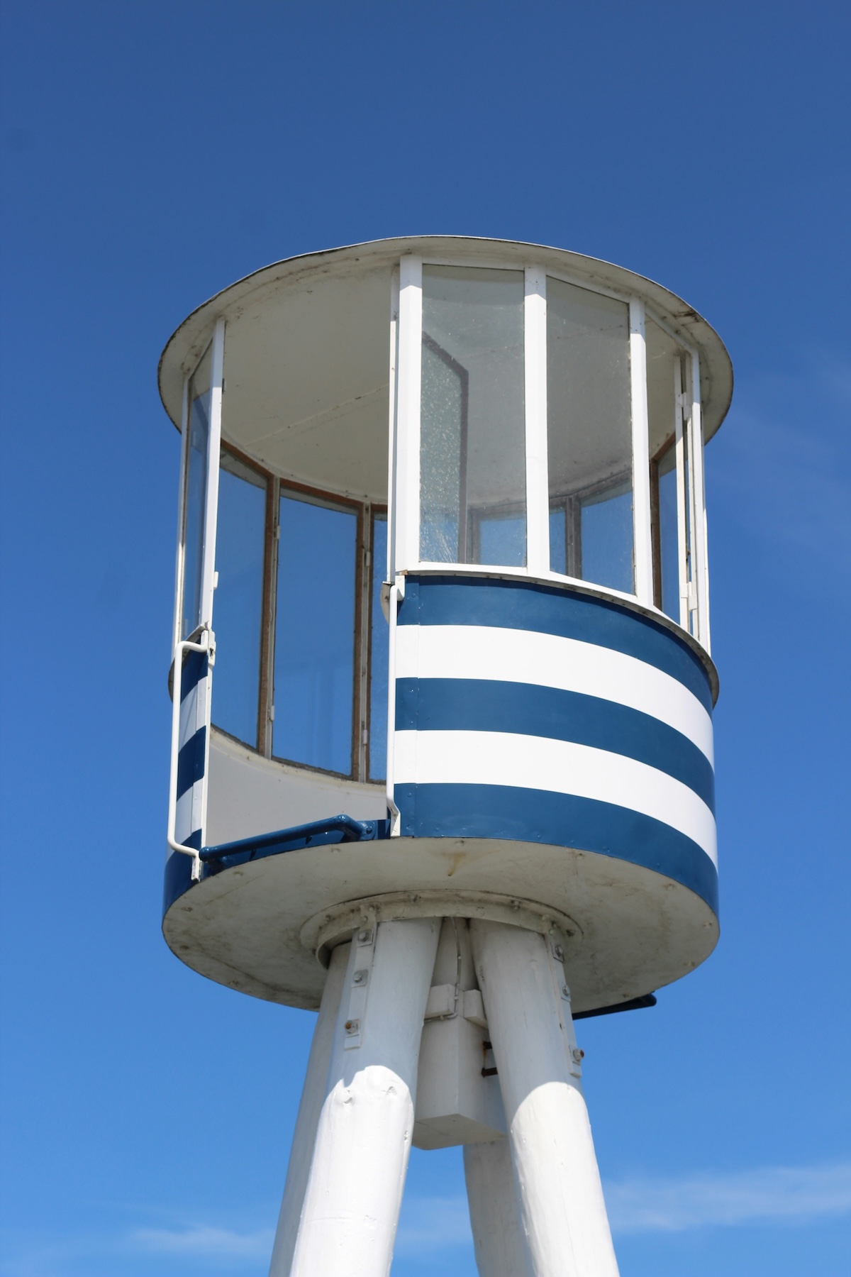 Close-up of Arne Jacobsen's blue-and-white striped Bellevue Beach lifeguard tower against a clear blue sky.