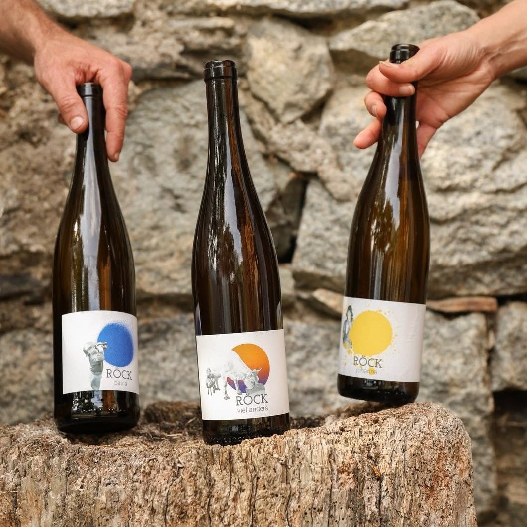 Three bottles of Röck wine, paula, viel anders and johanna, standing on a weathered tree stump against a dry stone wall, Villanders, South Tyrol | The Aficionados
