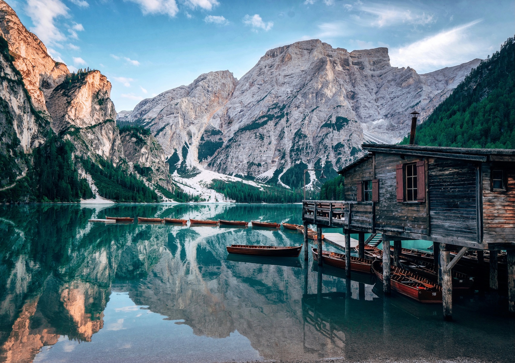 Wooden boathouse and rowing boats reflected in the turquoise water of Lago di Braies beneath the Dolomites, South Tyrol