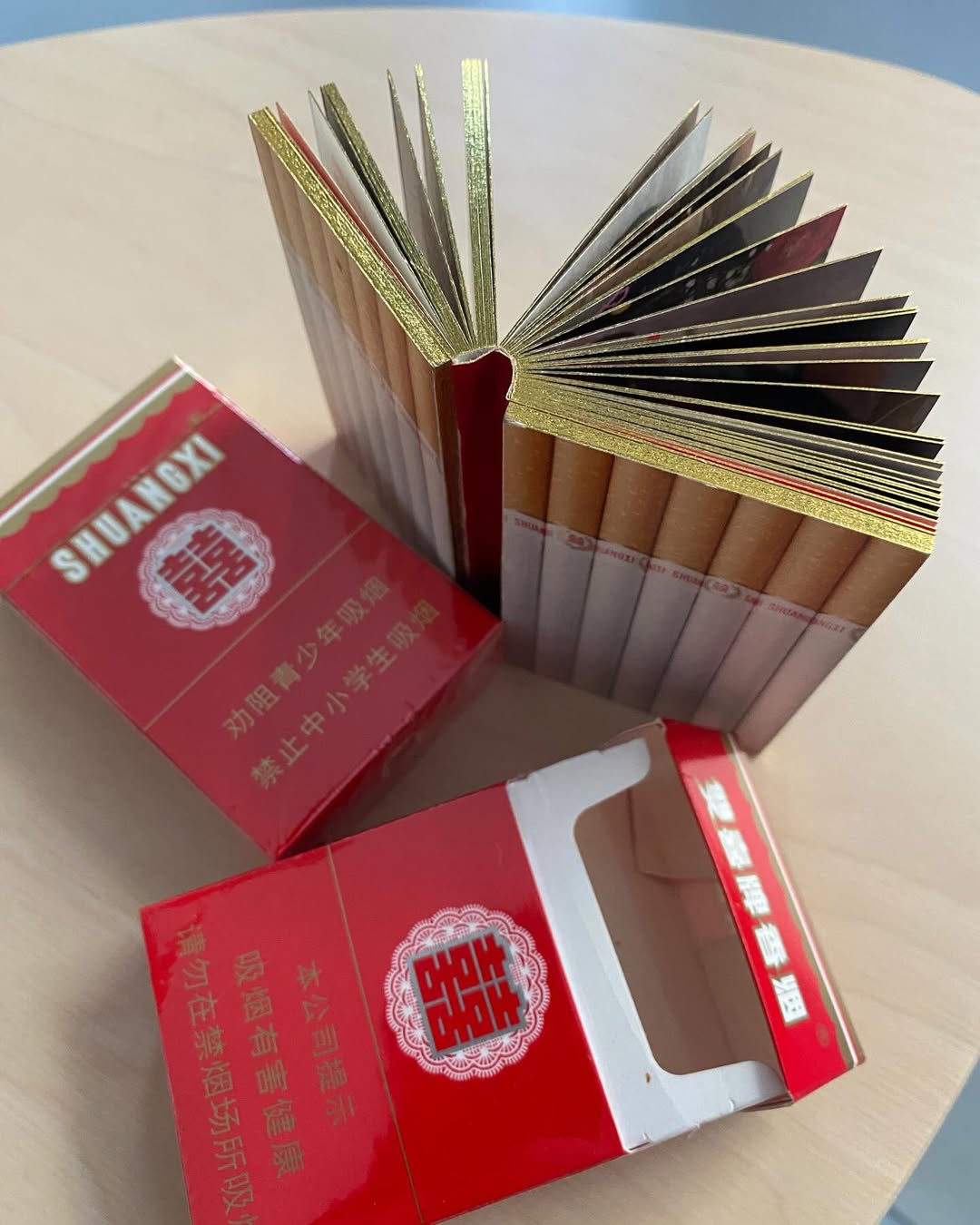The Thomas Sauvin cigarette-pack book open to show gilded page edges beside its Shuangxi box, an art object at Softcover.