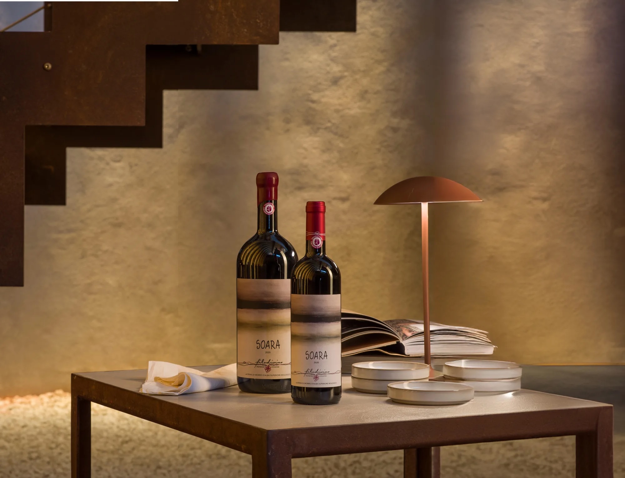 Two bottles of Filodivino Soara Lacrima di Morro d'Alba styled on a table with a copper lamp and open book, Le Marche Italy