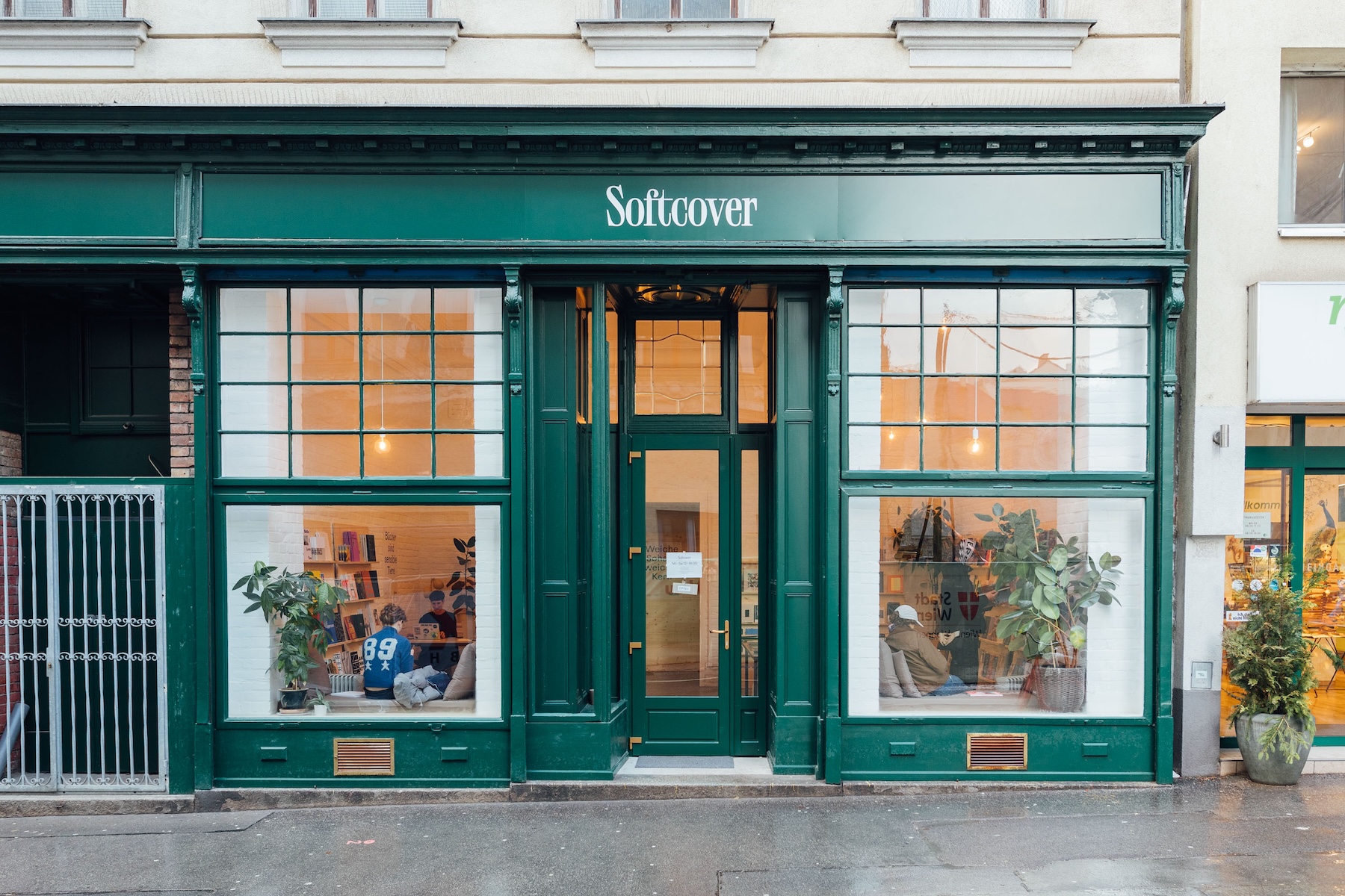 Green Art Nouveau shopfront of Softcover, an independent magazine shop in Vienna, with customers reading in the lit windows.