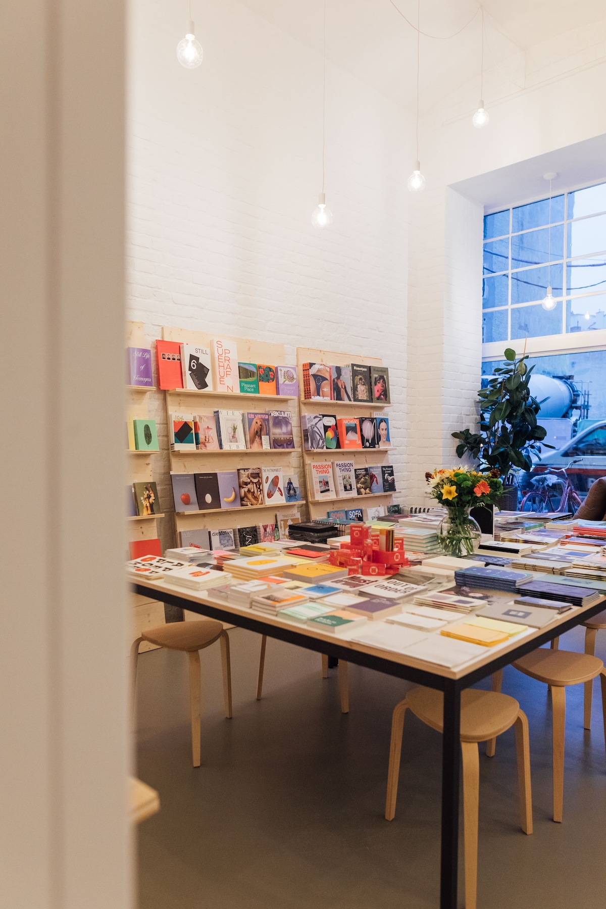 Interior of Softcover Vienna: white brick walls, wall-mounted magazine shelves, a central browsing table and fresh flowers.