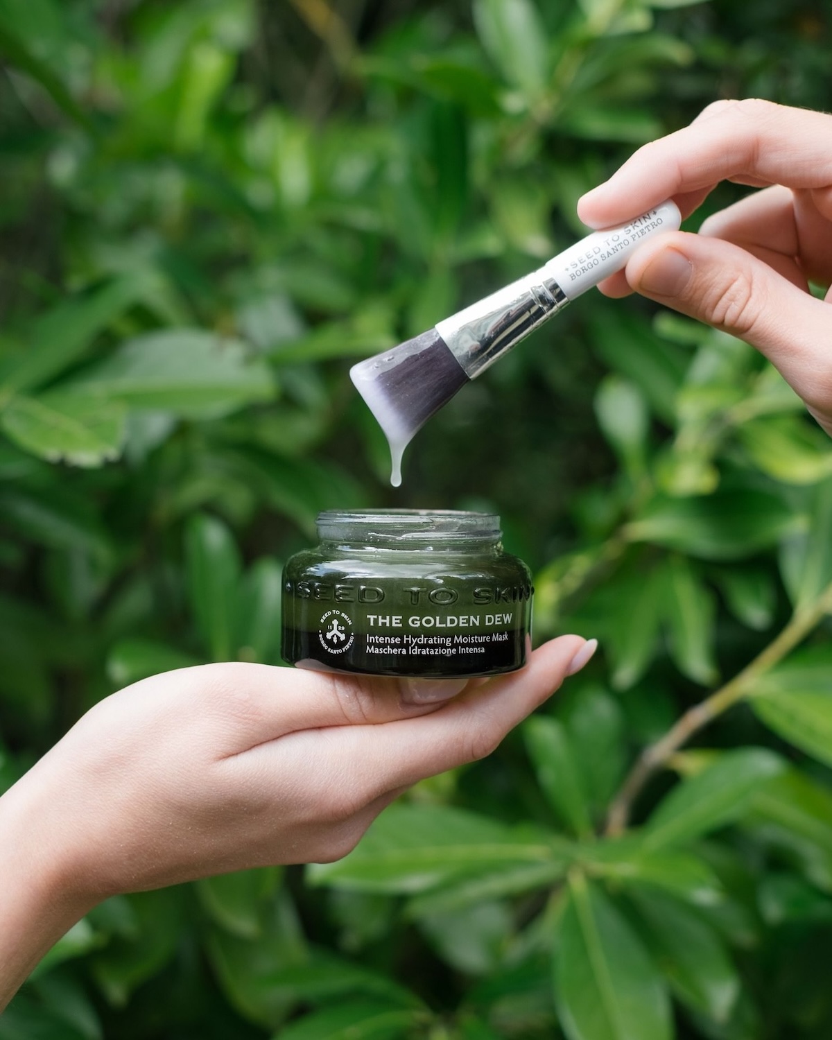Seed to Skin Tuscany The Golden Dew intense hydrating moisture mask in a deep green glass jar with application brush against estate foliage, natural luxury skincare made in Chiusdino Italy | The Aficionados