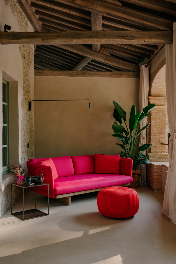 A cherry-pink sofa and red pouffe beneath beamed ceilings in a palette-led room at Vocabolo Moscatelli, Umbria.